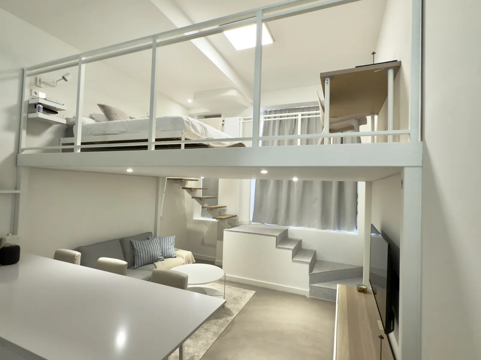 Loft con altillo de barandilla blanca sobre la zona de estar y escalera de madera