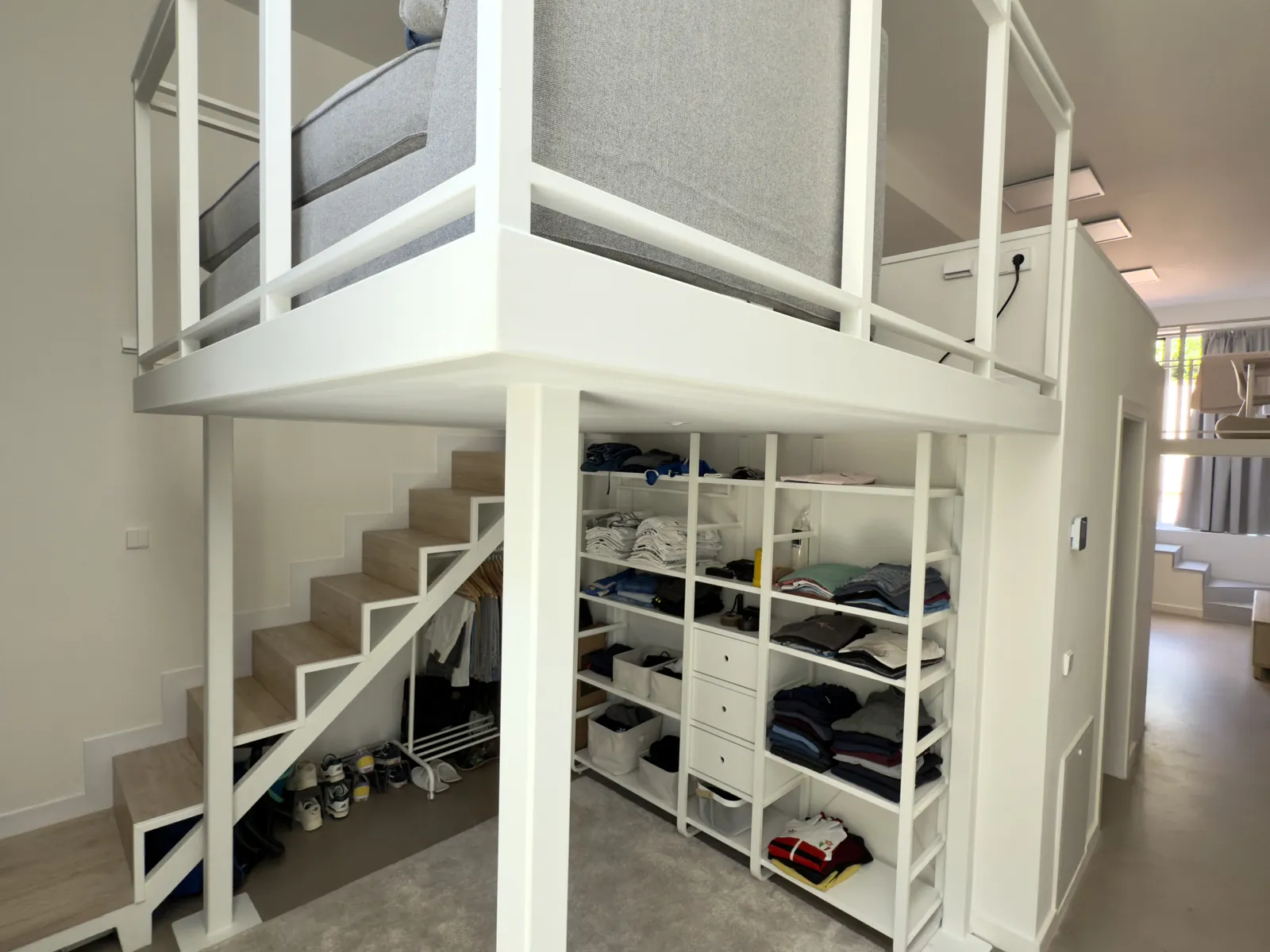 Escalera de madera con almacenaje bajo el altillo de estructura blanca