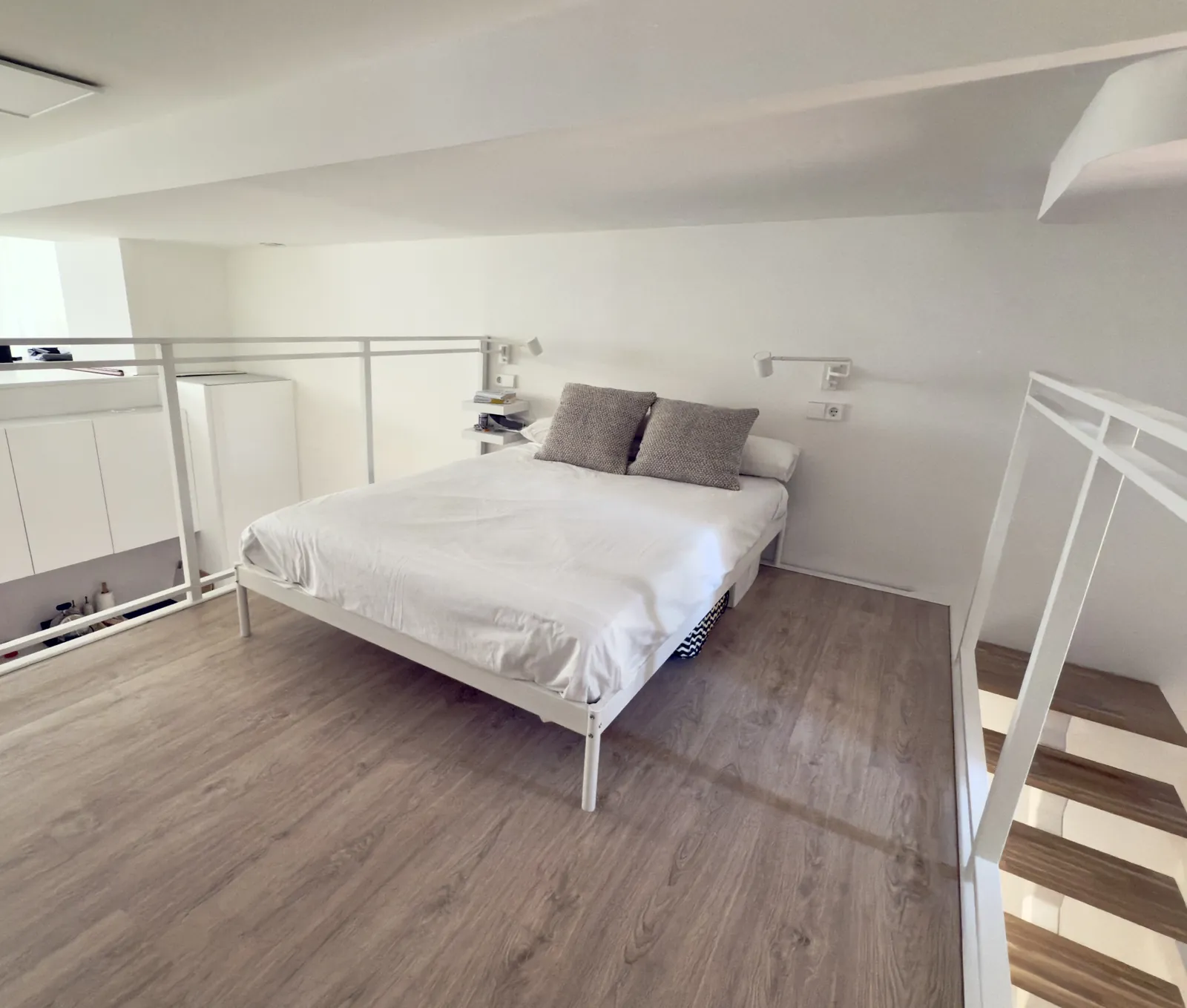 Dormitorio en el altillo con cama, suelo laminado claro y barandilla blanca