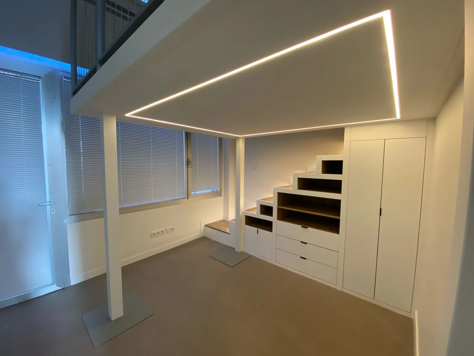 Escalera-almacenaje con cajones blancos y perfil de luz lineal en el techo bajo el altillo