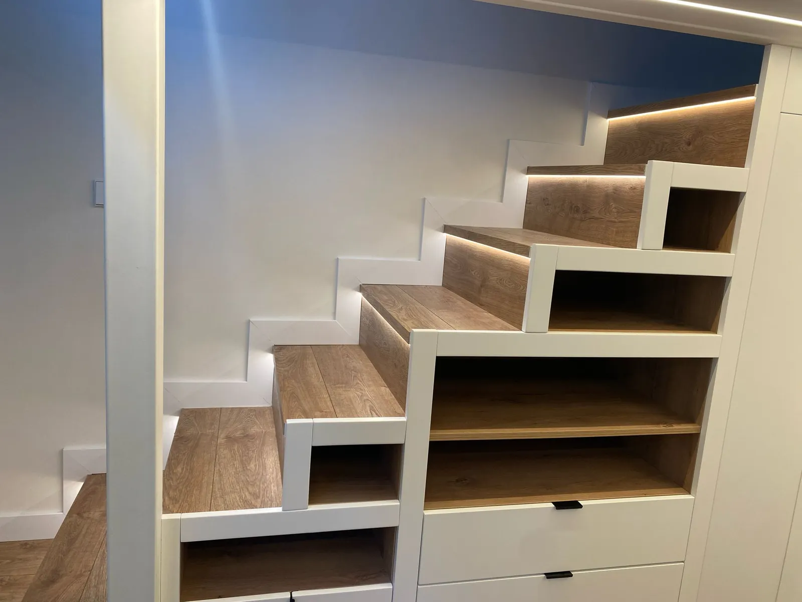 Detalle de peldaños de madera con cajones y tira LED en la escalera del altillo