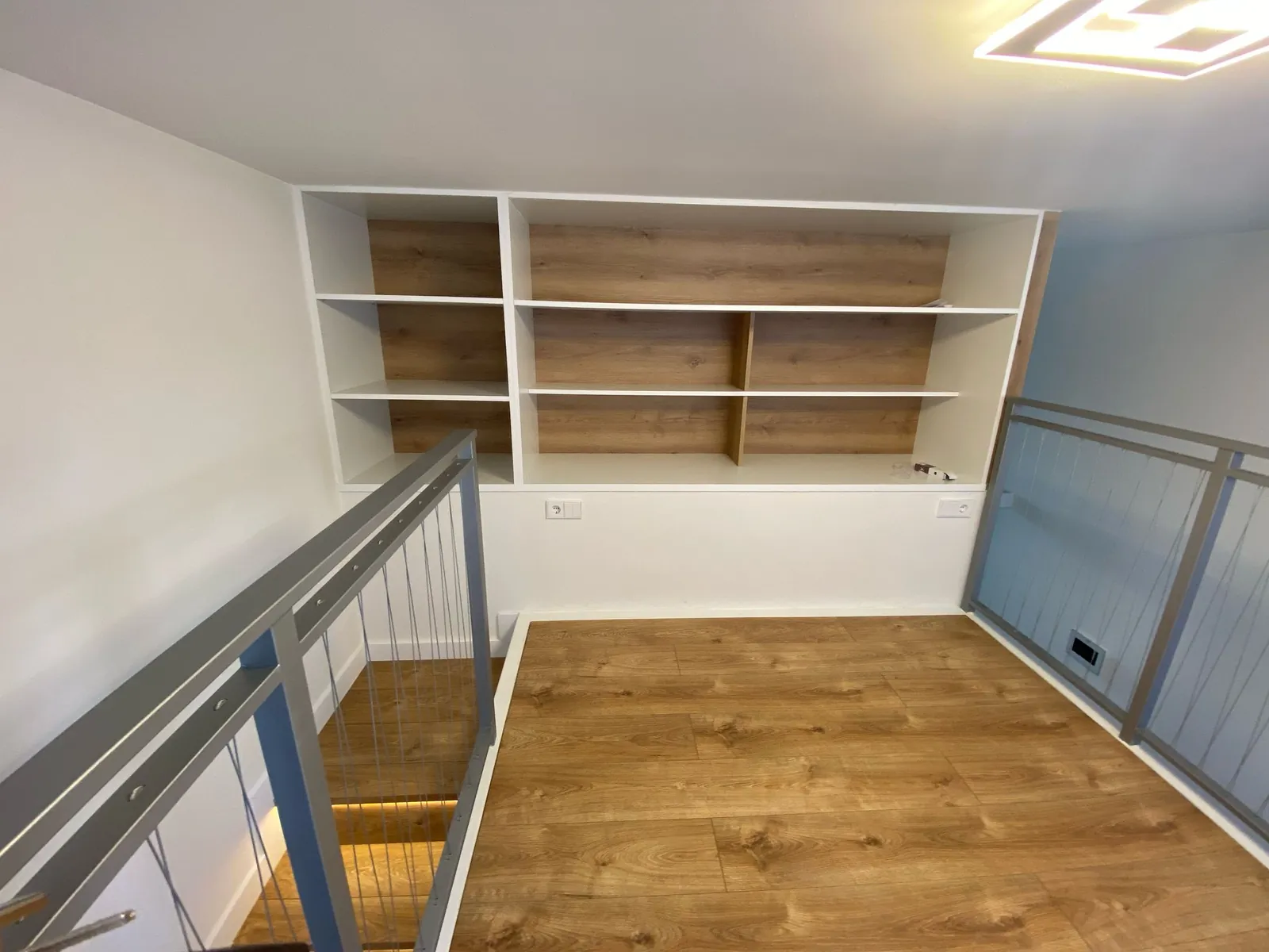 Planta del altillo con suelo de madera y estanterías empotradas blancas y madera