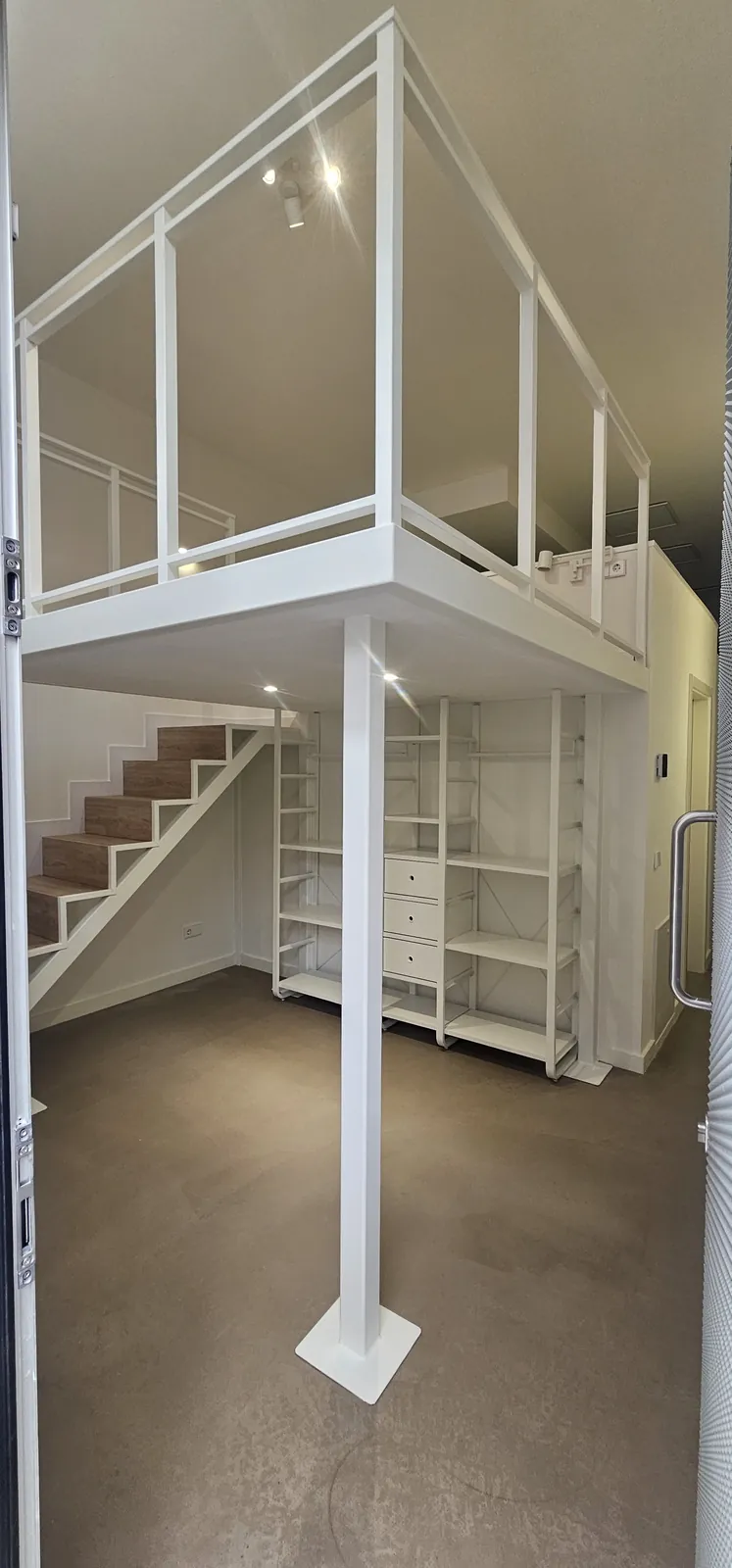 Altillo blanco con barandilla metálica sobre pilar y escalera de madera