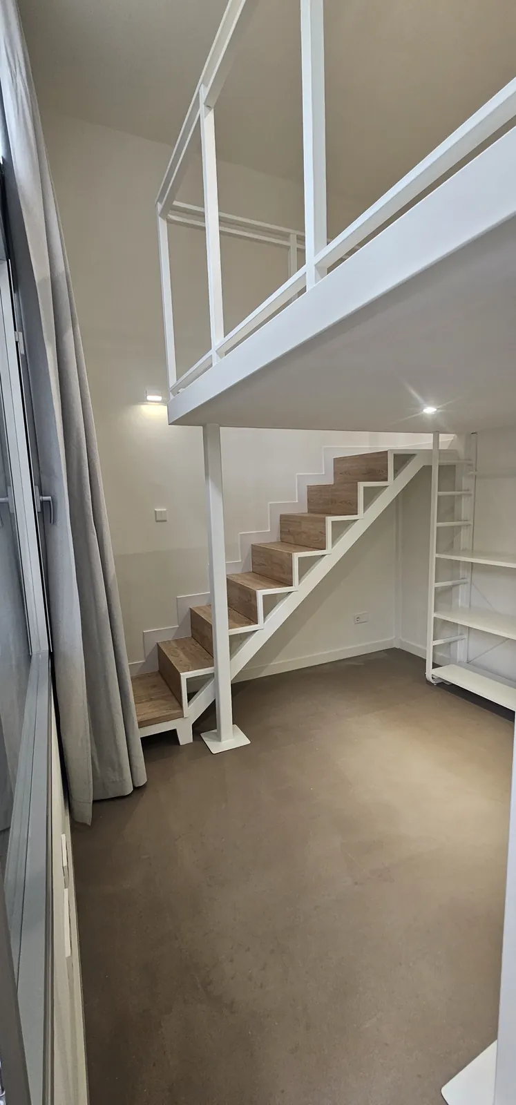 Escalera de madera y estanterías bajo el altillo de estructura blanca