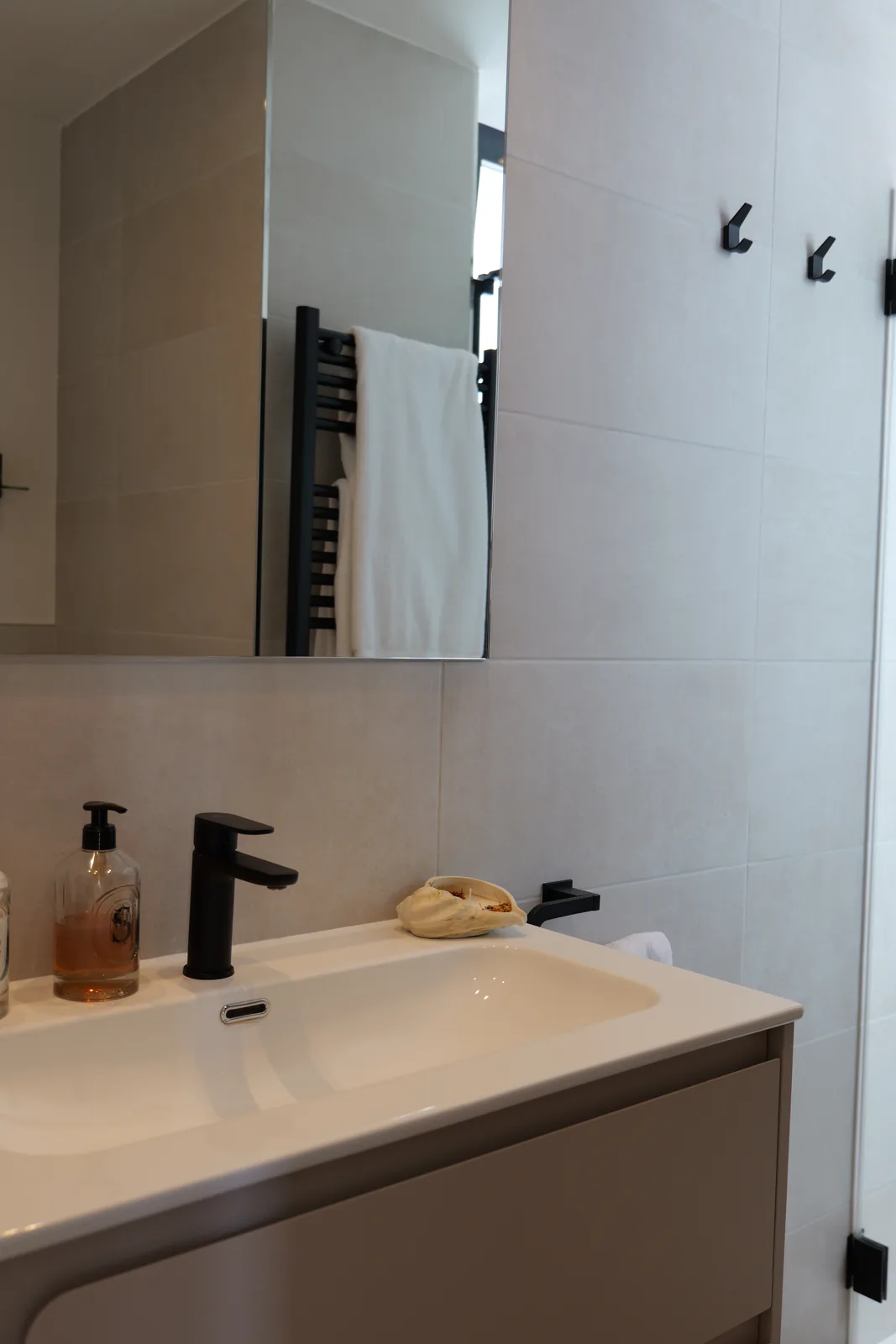 Baño con lavabo integrado sobre mueble en tono topo, grifería negra y revestimiento cerámico claro