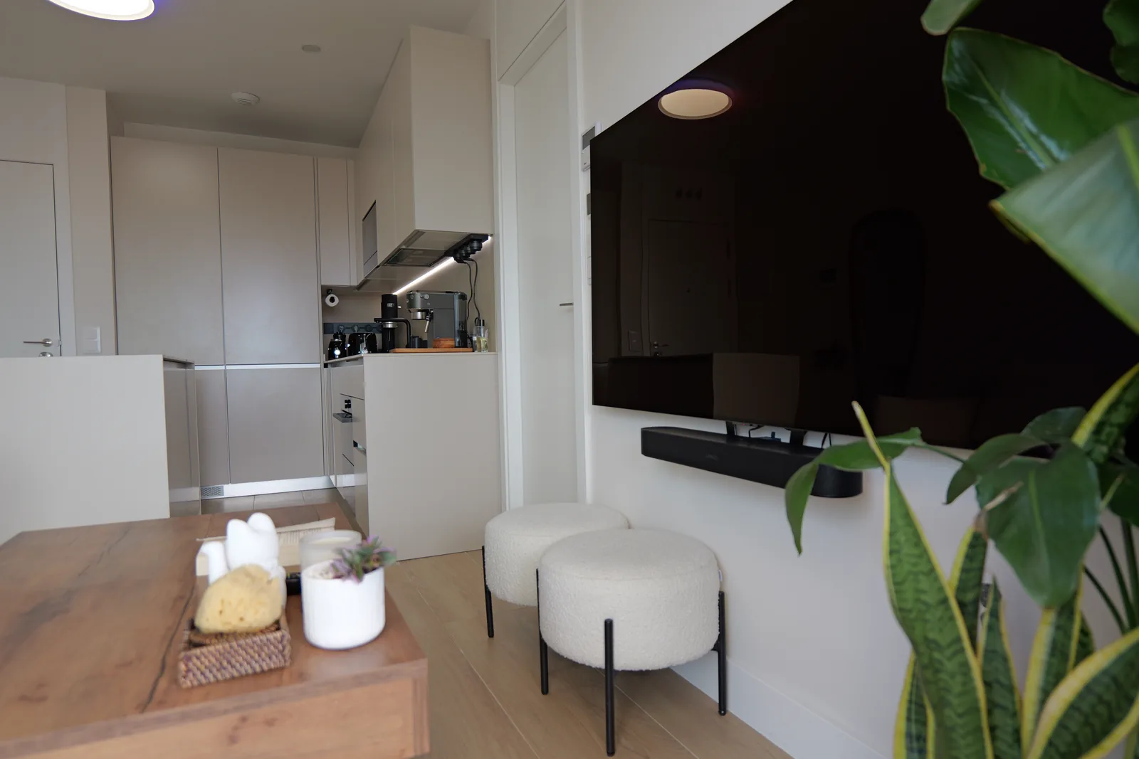 Cocina abierta en tonos crema con armarios columna y suelo de tarima clara vista desde el salón