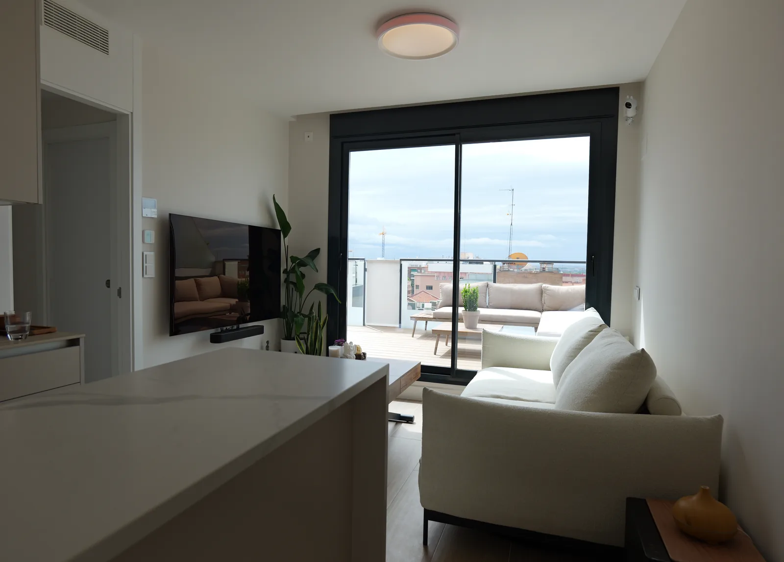 Salón-cocina abierto con isla de encimera blanca veteada y gran ventanal corredero hacia la terraza