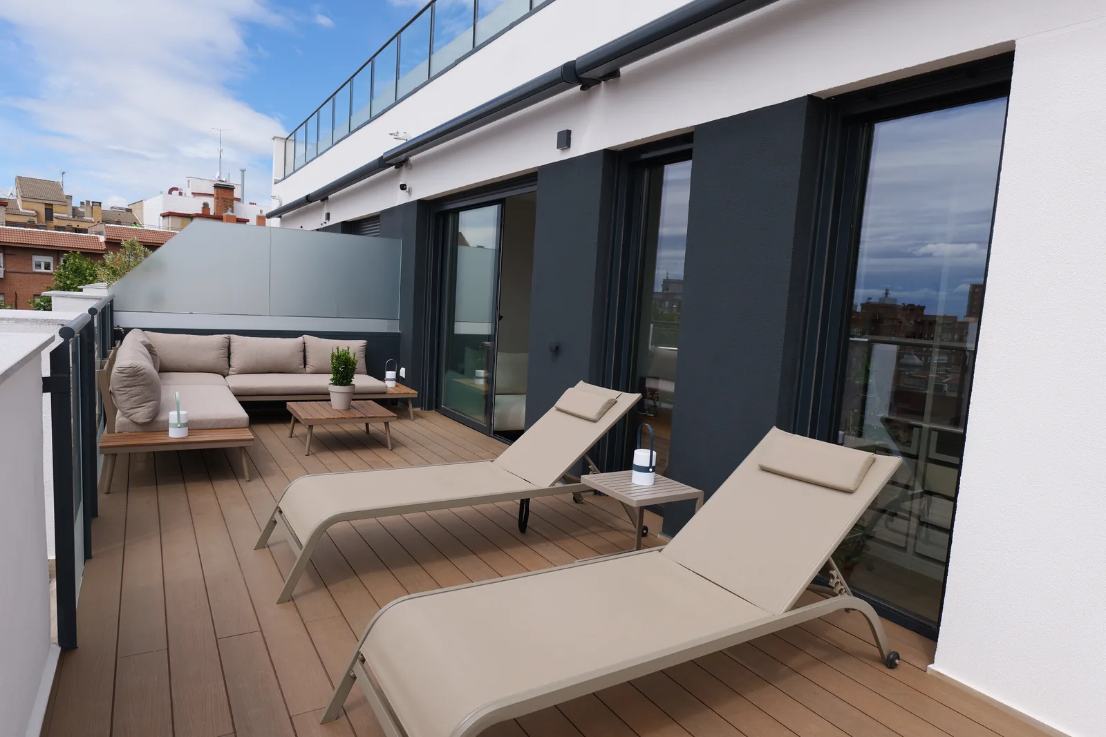 Terraza de ático con tarima de madera, tumbonas, sofá exterior y fachada en gris antracita