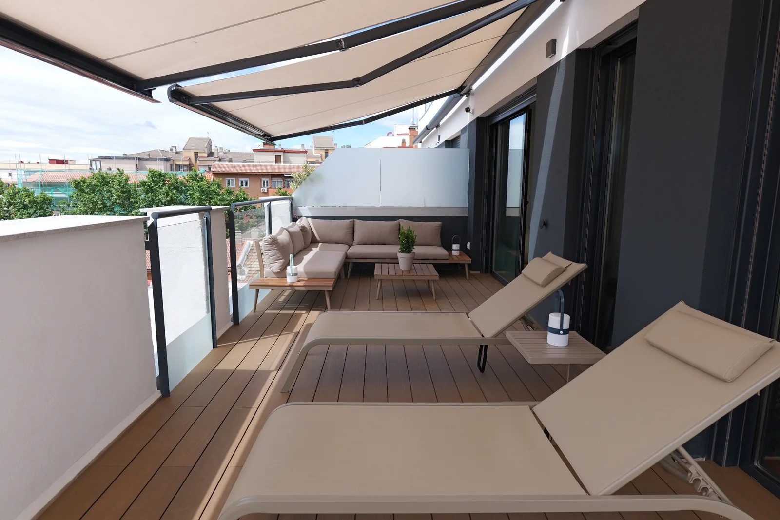 Vista bajo el toldo de la terraza con tumbonas, tarima de madera y zona de sofá al fondo