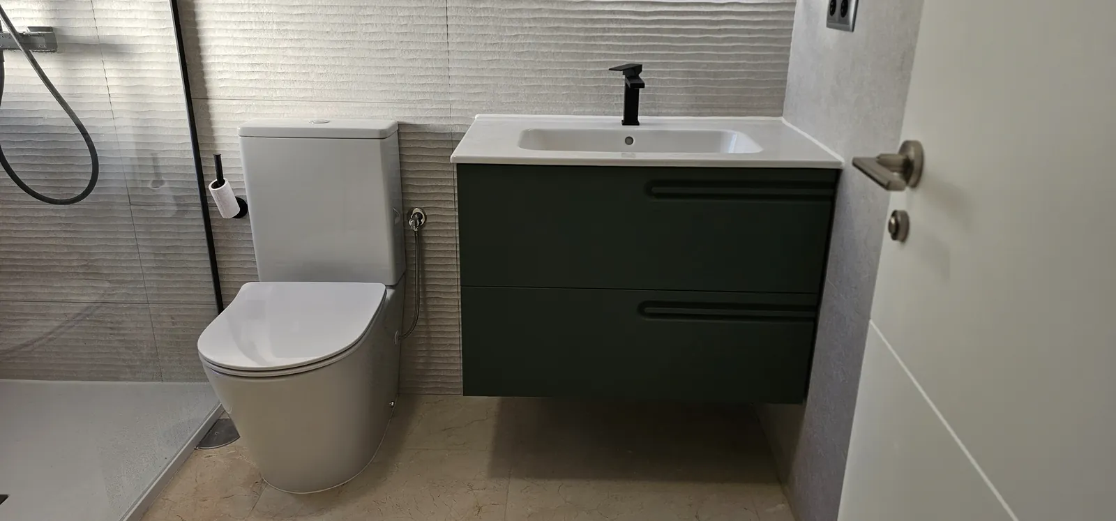Mueble de lavabo suspendido verde oscuro con grifo negro junto al inodoro