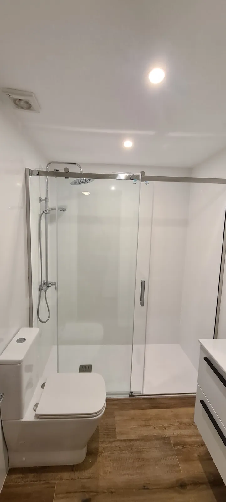 Baño blanco con ducha de mampara corredera de vidrio e inodoro