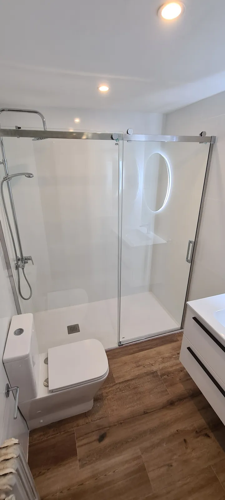 Ducha con mampara de vidrio y alicatado blanco junto a mueble de lavabo