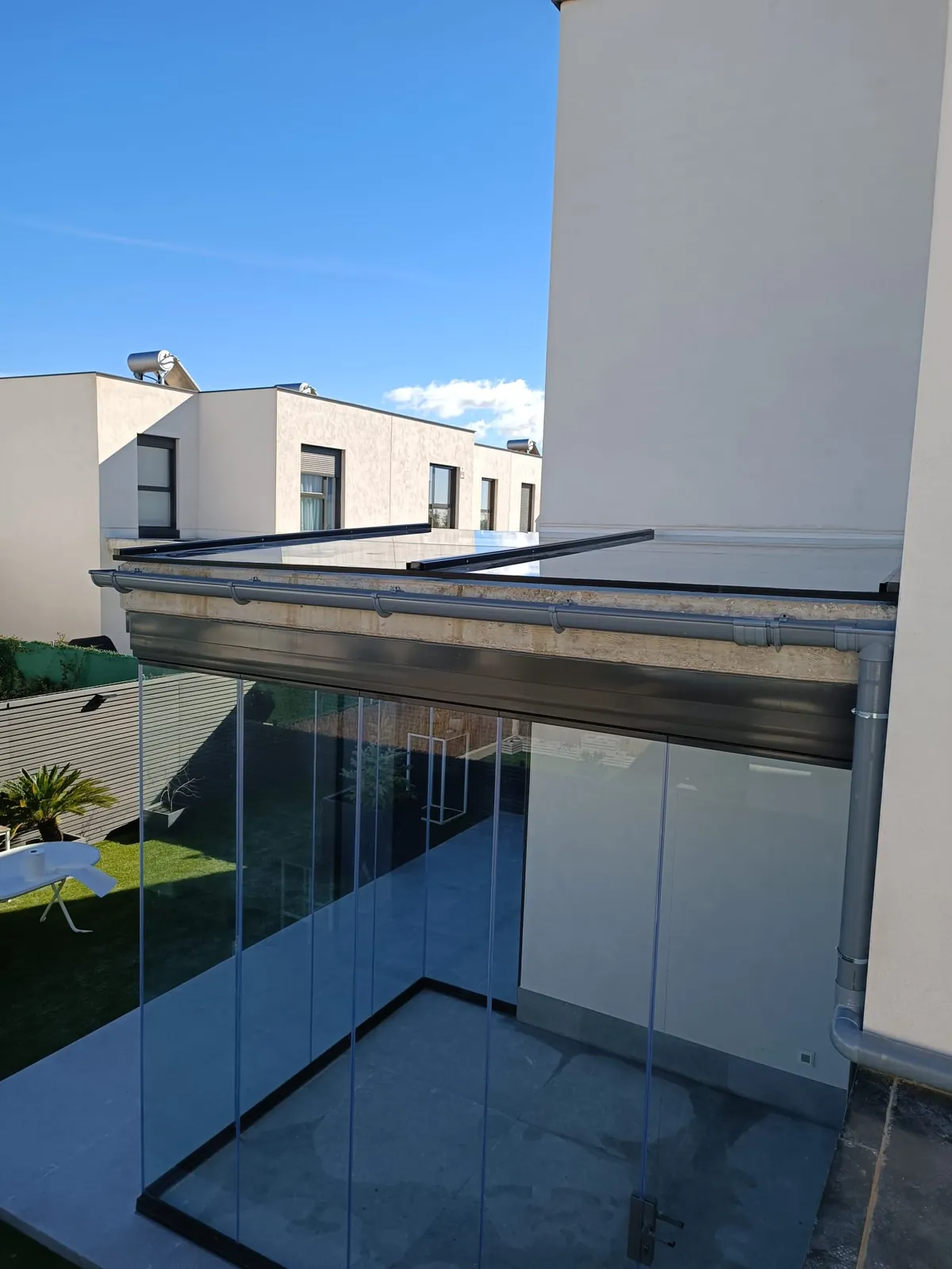 Porche cerrado con cortinas de vidrio y perfilería negra bajo pérgola