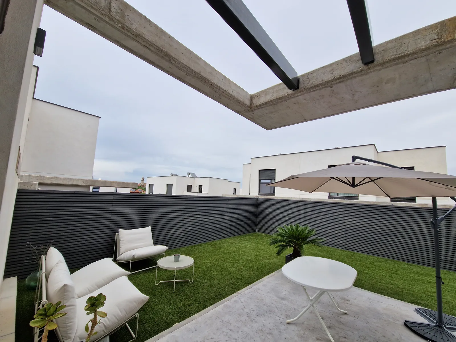 Patio con valla de lamas gris oscuro, césped artificial y pérgola de hormigón