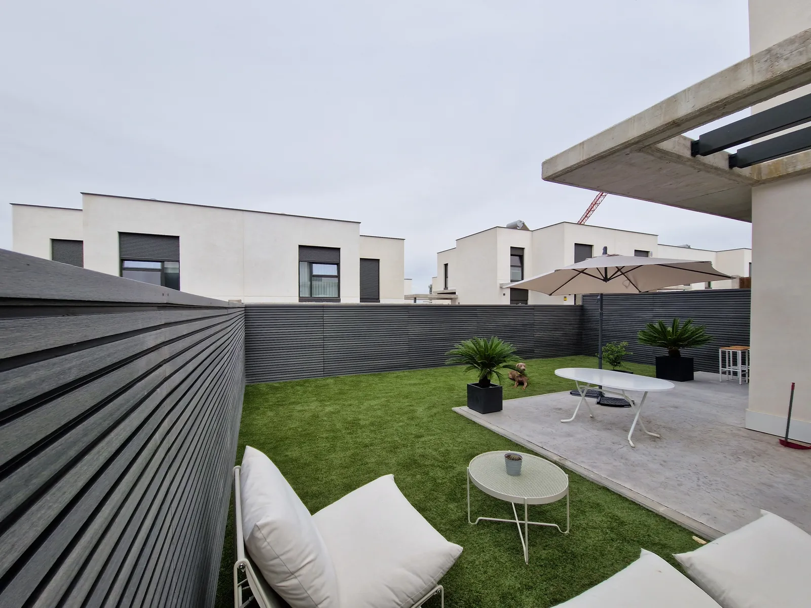 Patio terminado con césped artificial, pavimento claro y valla de lamas