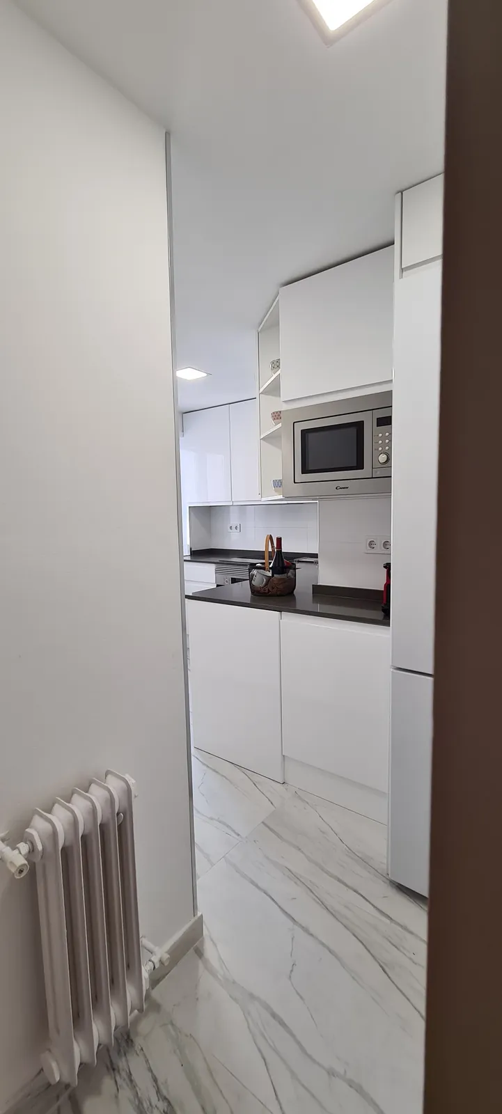 Vista de la cocina blanca desde la puerta con suelo imitación mármol