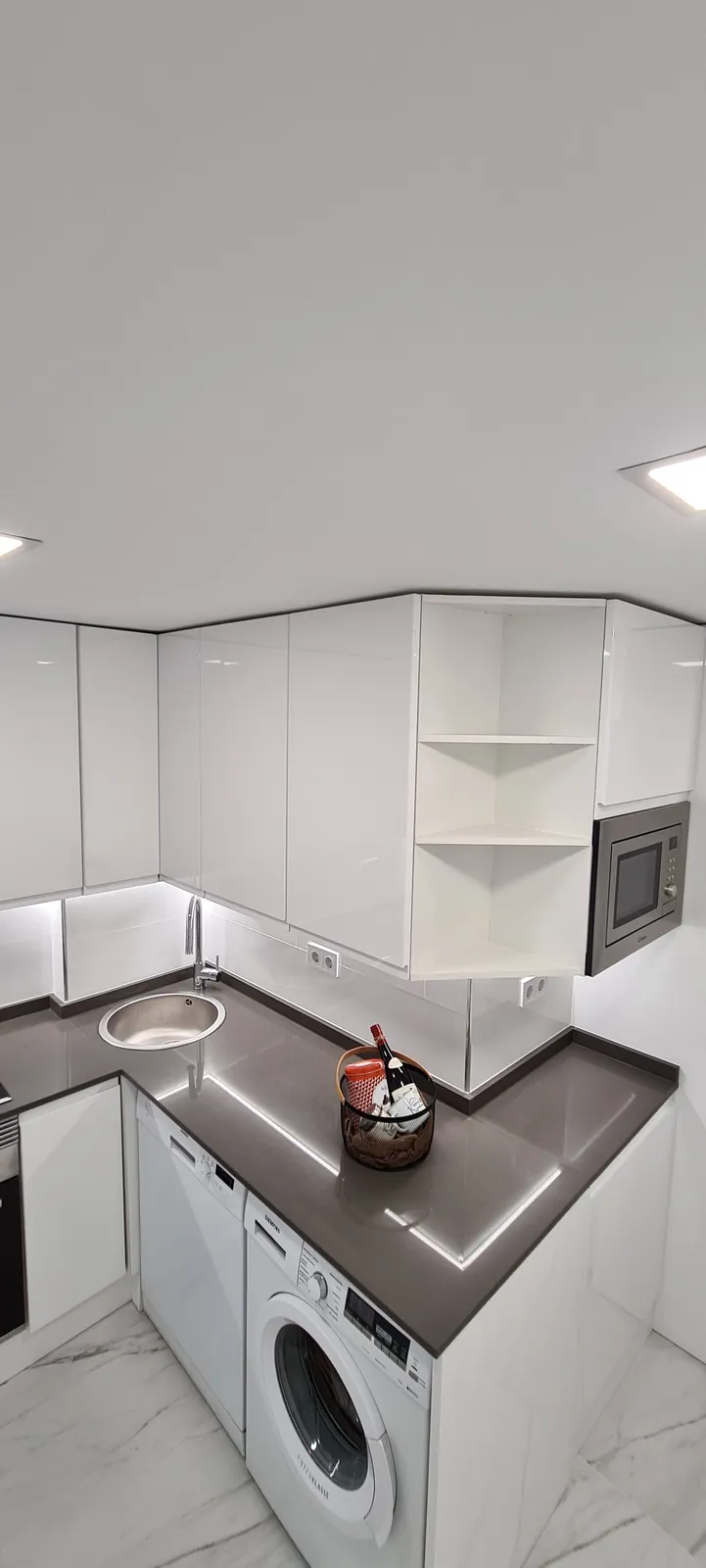 Cocina en L con lavadora integrada, encimera gris y luz LED bajo muebles