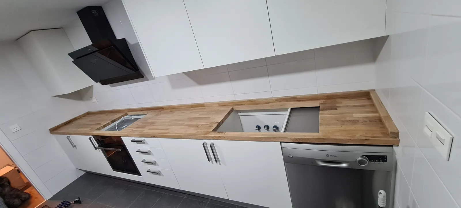 Cocina lineal con muebles blancos, encimera de madera y campana negra
