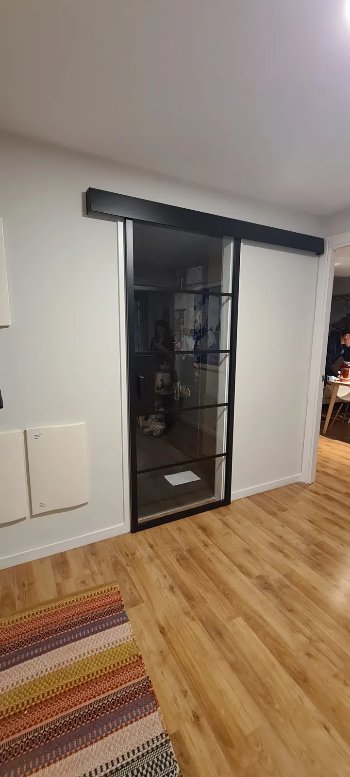 Puerta corredera de vidrio con perfil negro y guía vista instalada en el pasillo