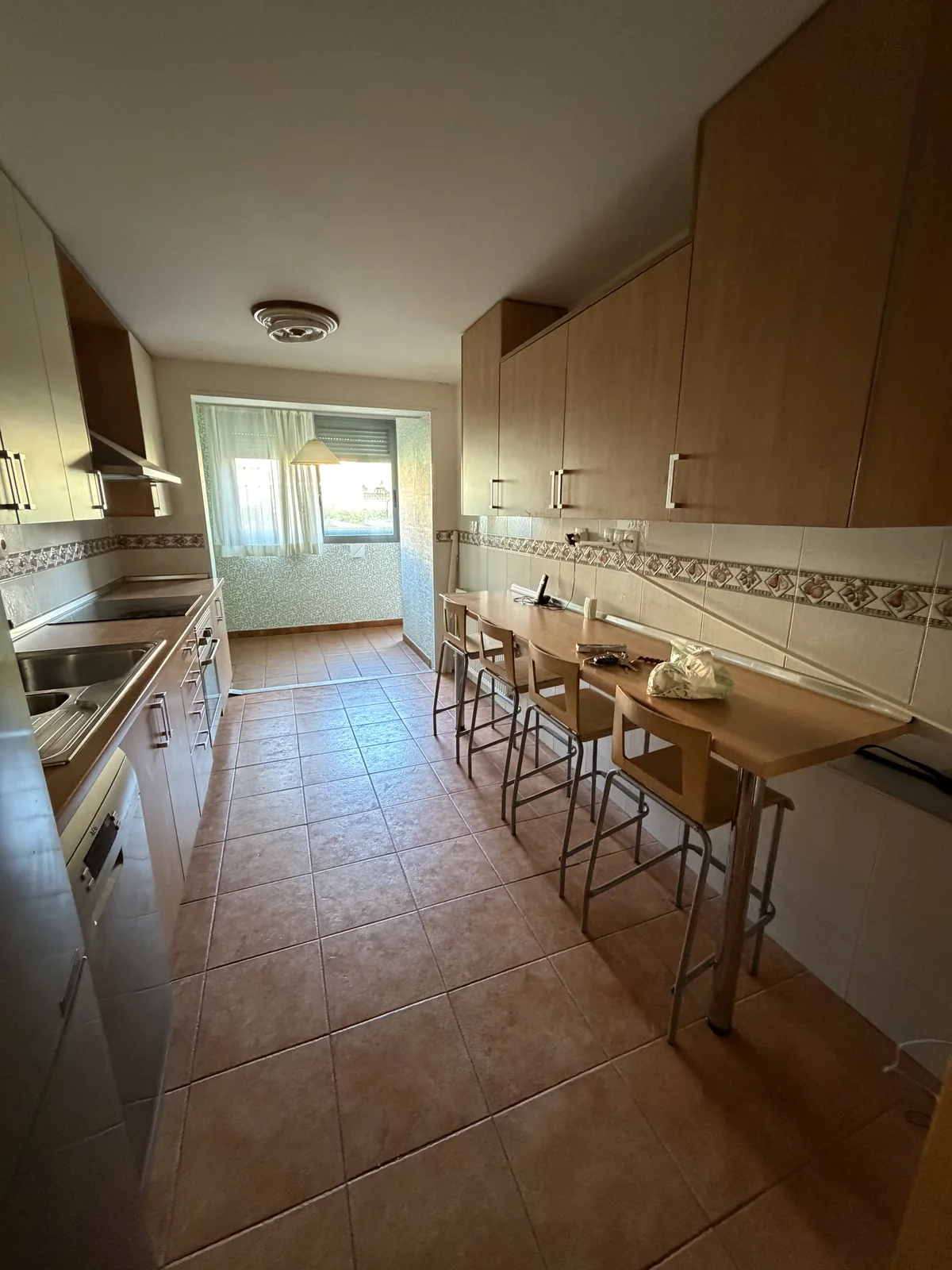 Cocina antes de la reforma, con muebles de madera clara, barra con taburetes y suelo de barro