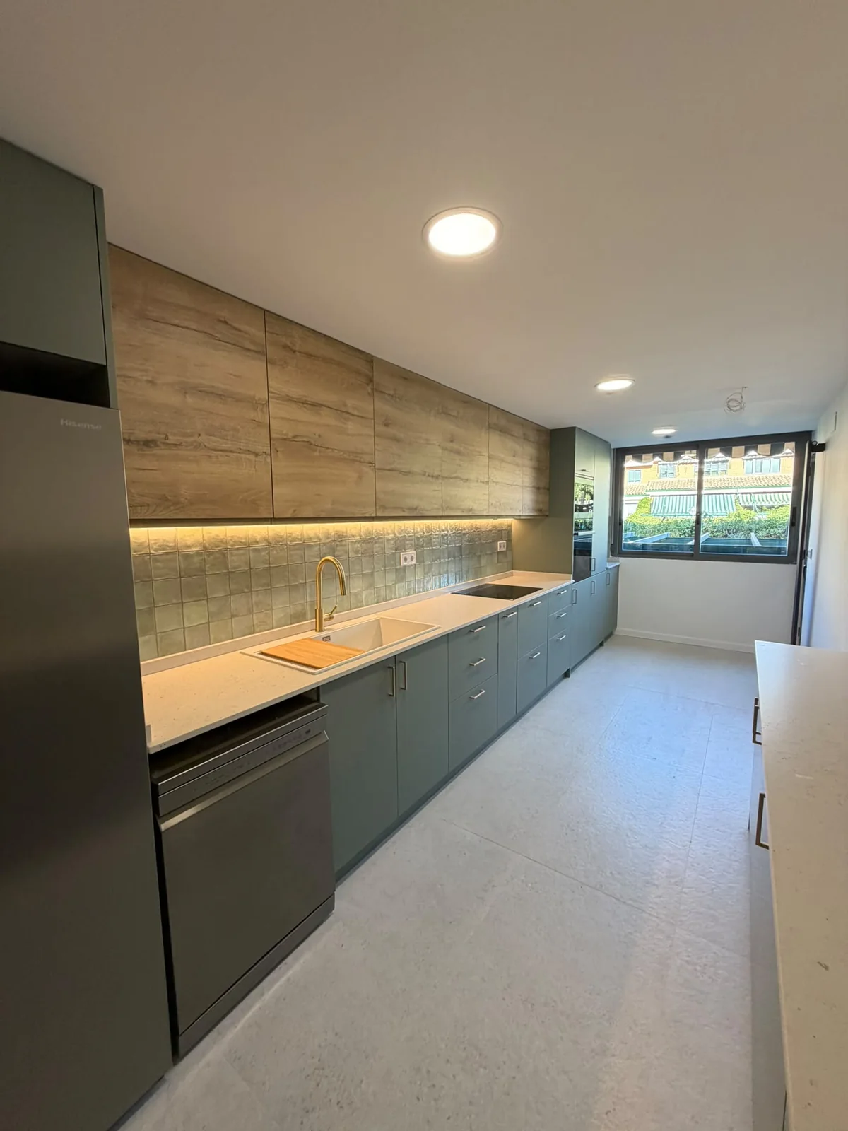Cocina reformada en verde y madera con frontal de azulejo verde artesanal, encimera clara y grifería dorada