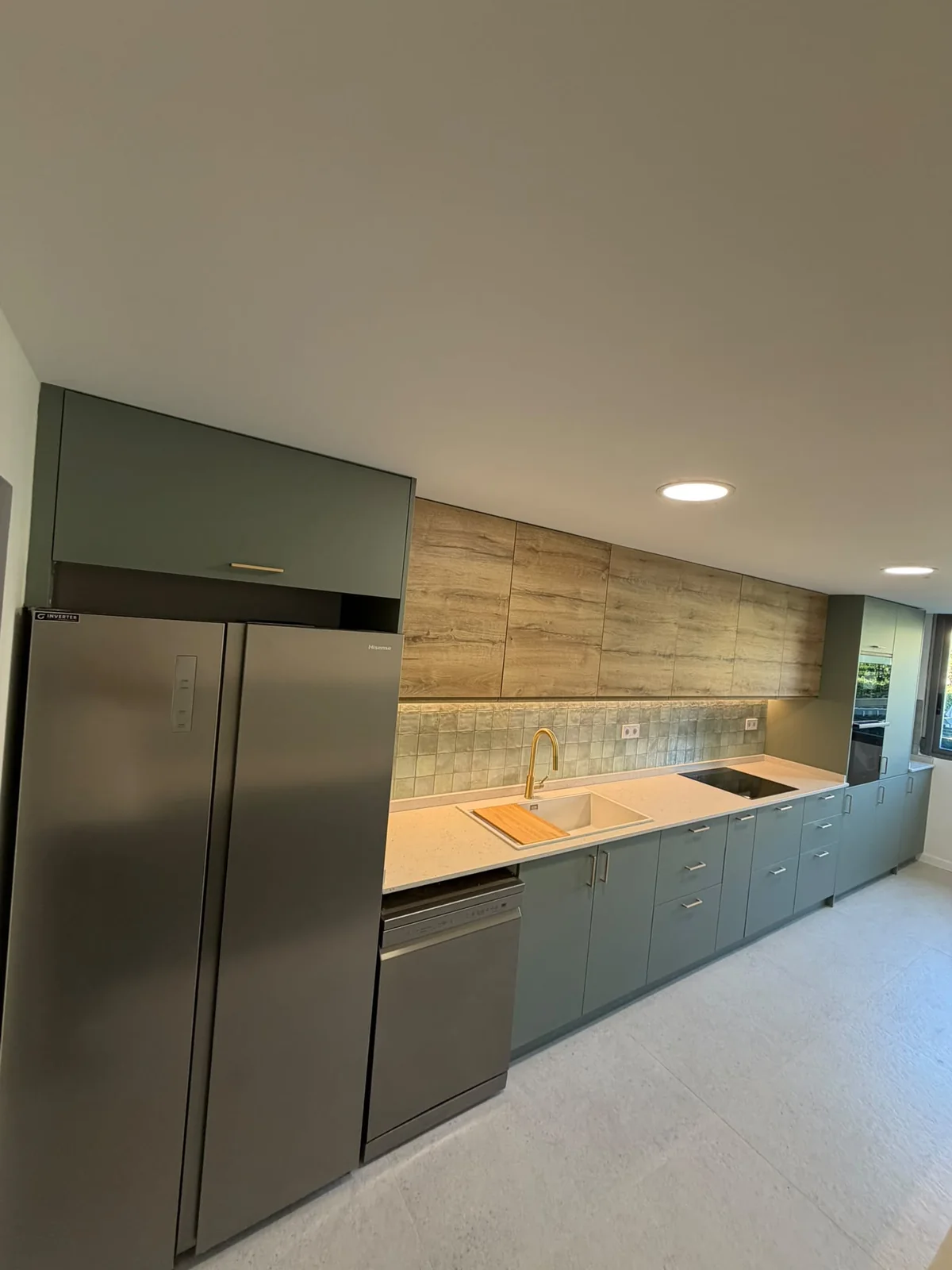Cocina lineal con muebles verdes, armarios altos en madera, frigorífico americano y lavavajillas