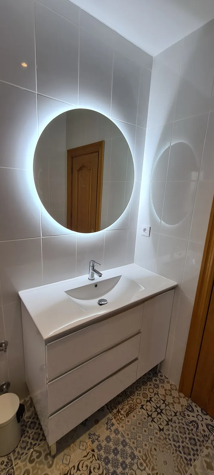 Lavabo blanco con espejo redondo retroiluminado y suelo de estilo hidráulico