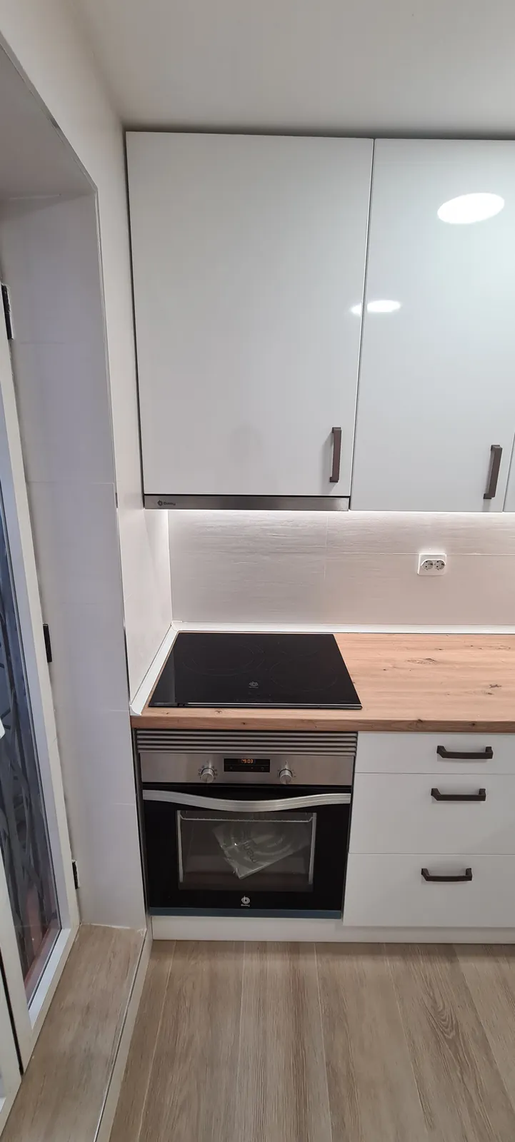 Cocina blanca con encimera de madera, placa de inducción y horno integrado