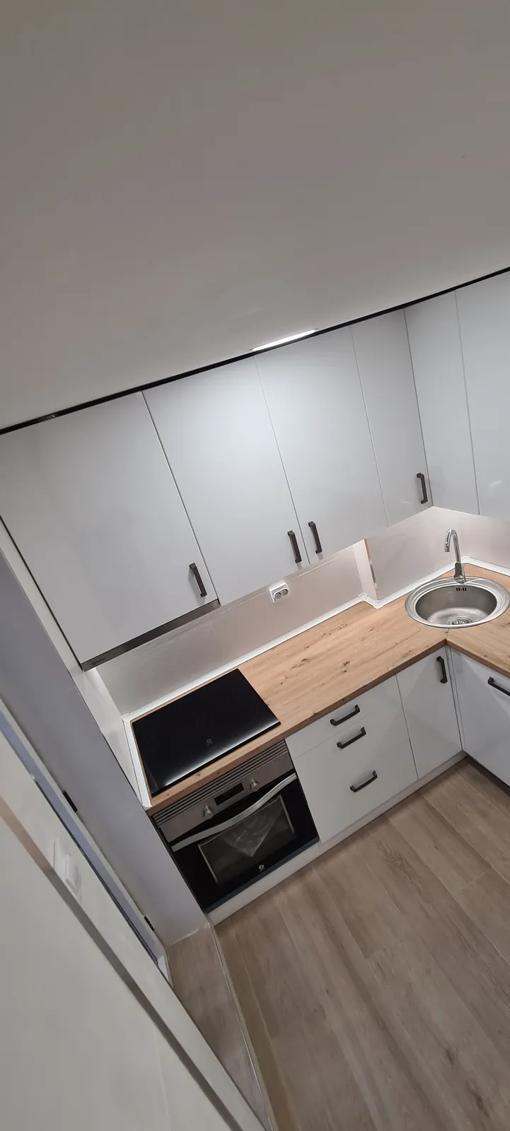 Rincón de cocina con muebles blancos, encimera de madera y fregadero