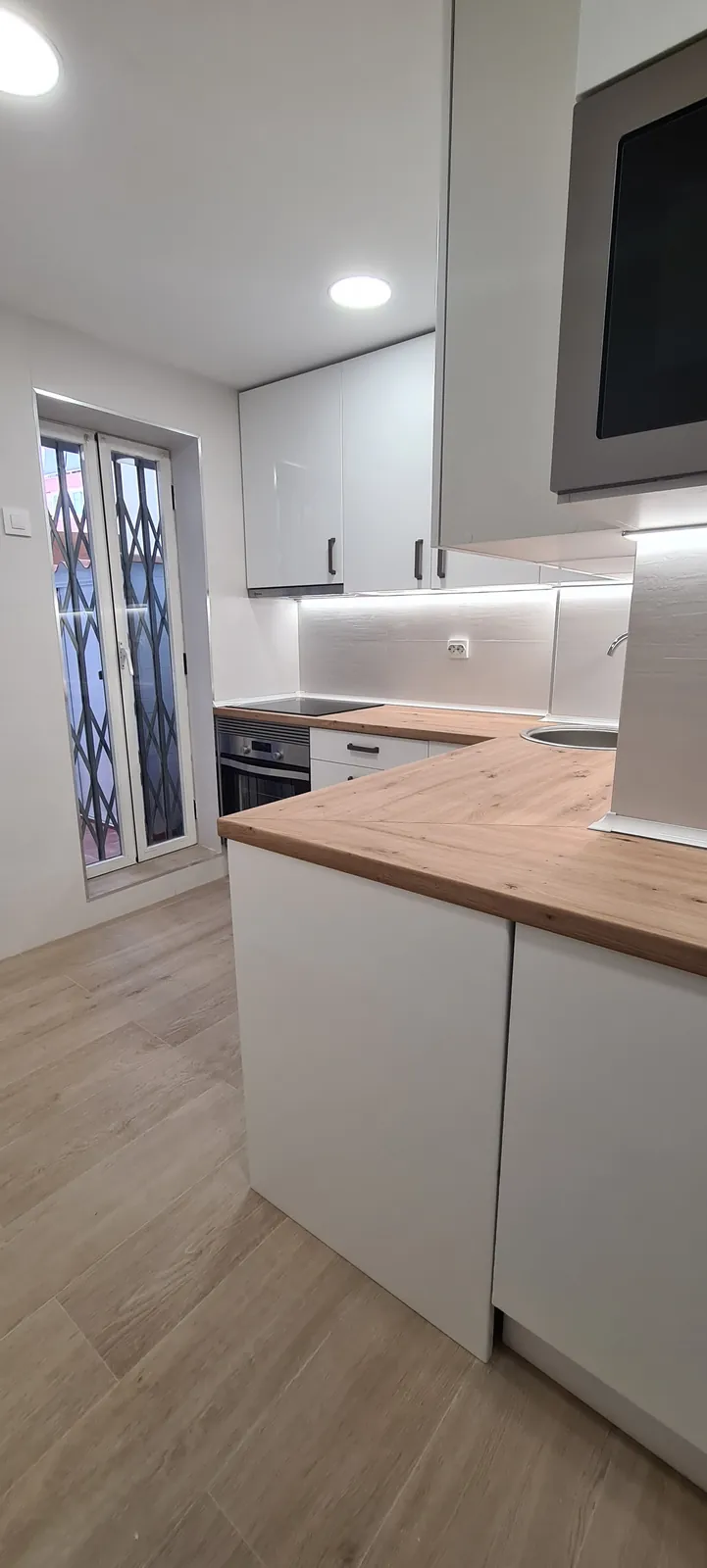 Cocina con península blanca, encimera de madera y suelo gris claro