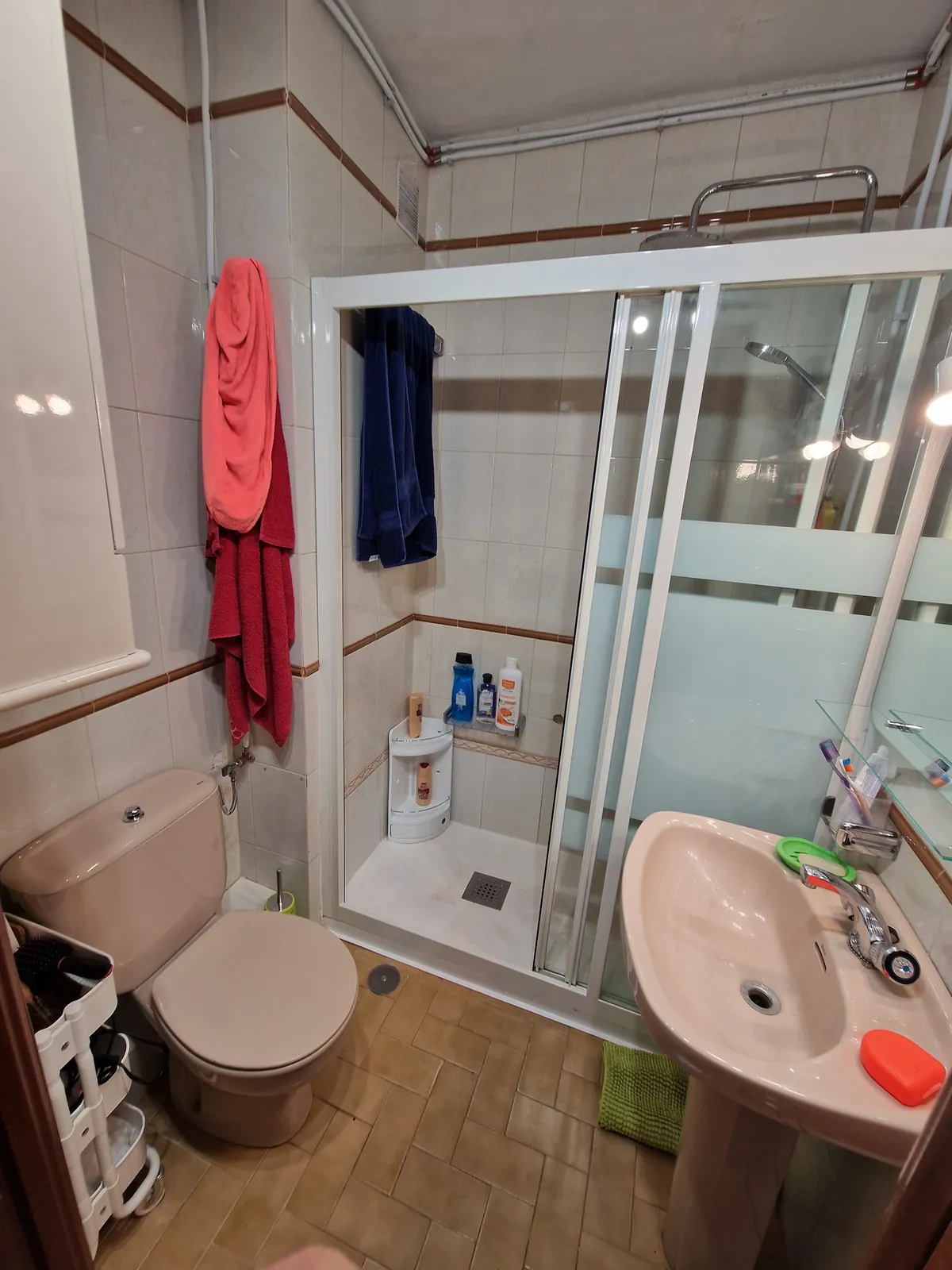 Baño antes de la reforma con sanitarios rosados y mampara antigua