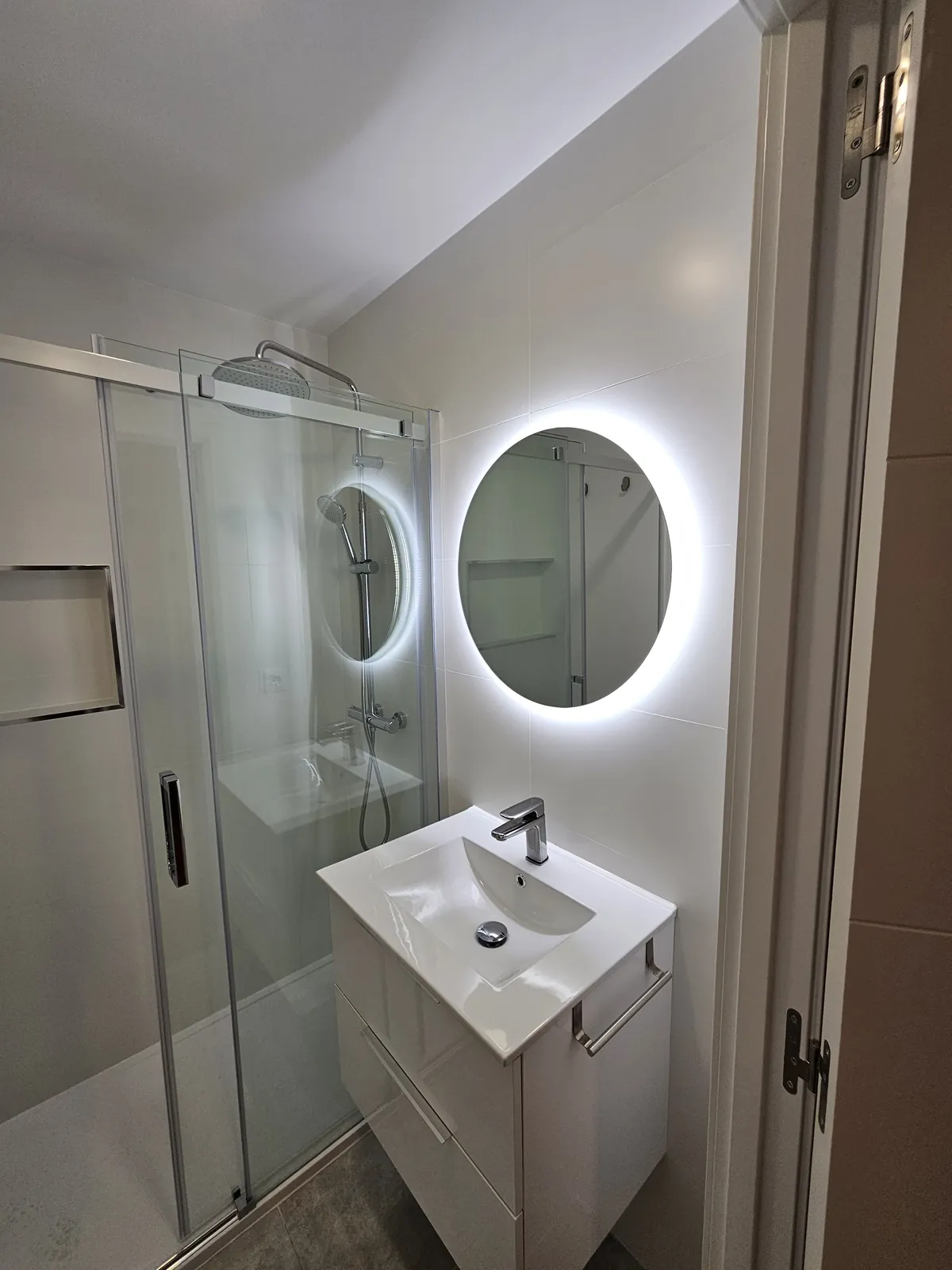 Ducha con hornacina y mampara de vidrio junto a mueble de lavabo blanco