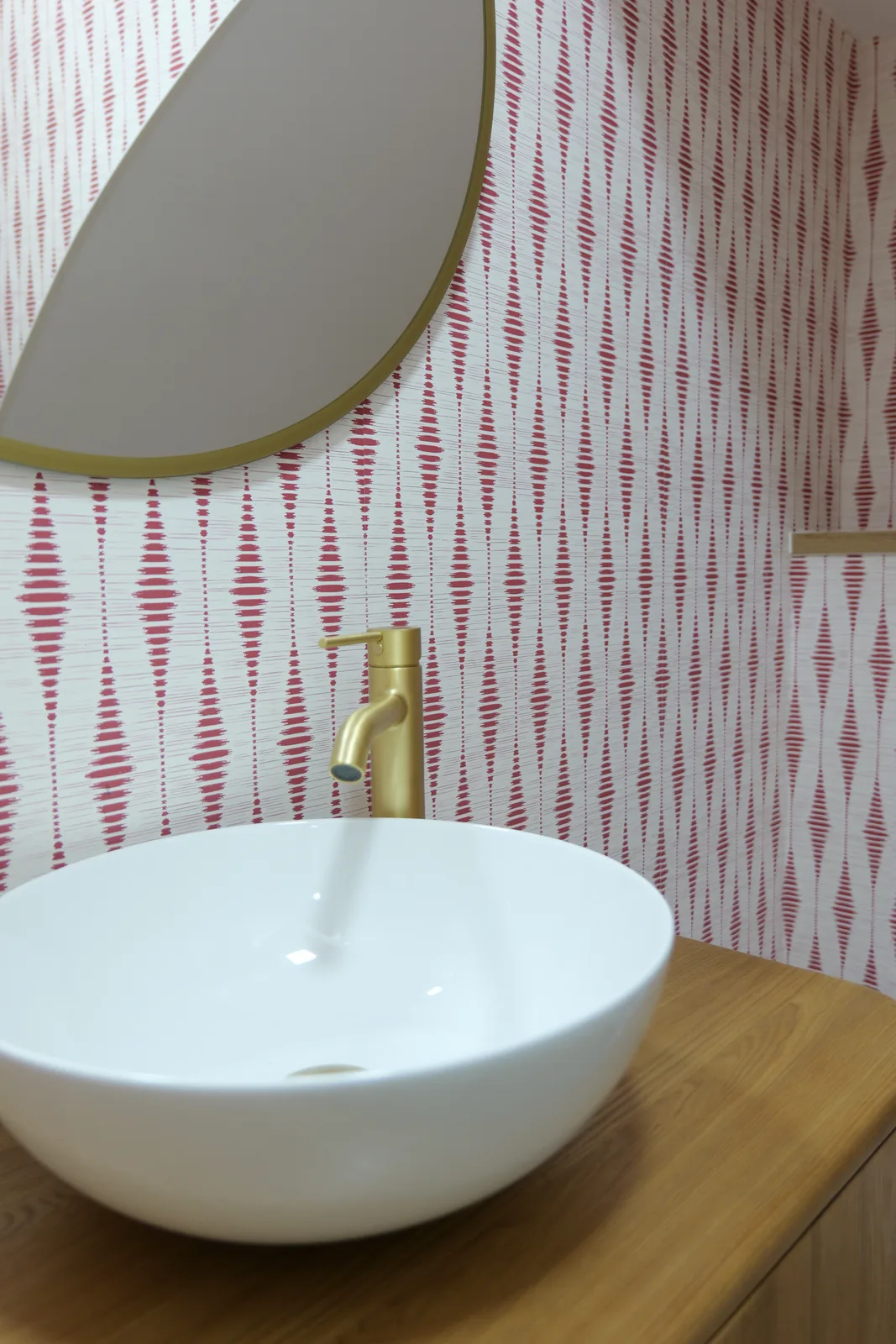 Detalle de lavabo de sobre encimera blanco con grifo dorado y espejo redondo