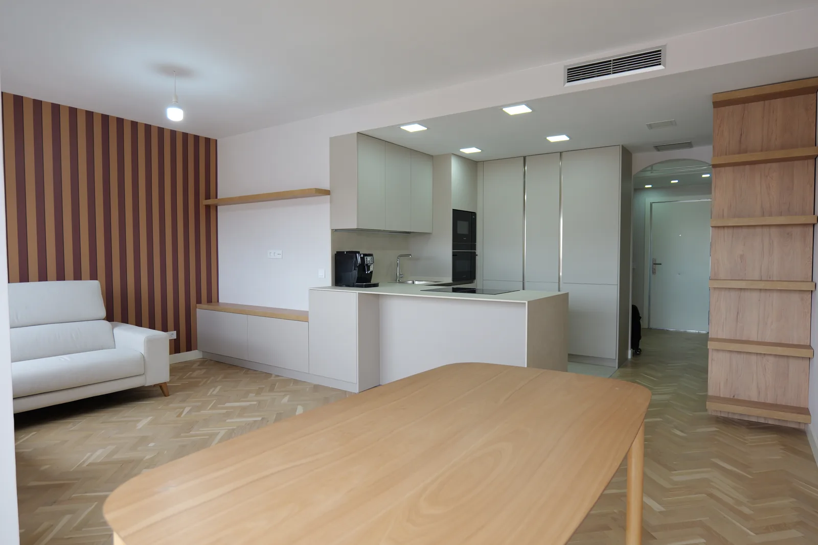 Salón-comedor abierto a la cocina con suelo de madera en espiga, pared de papel a rayas y mesa de madera