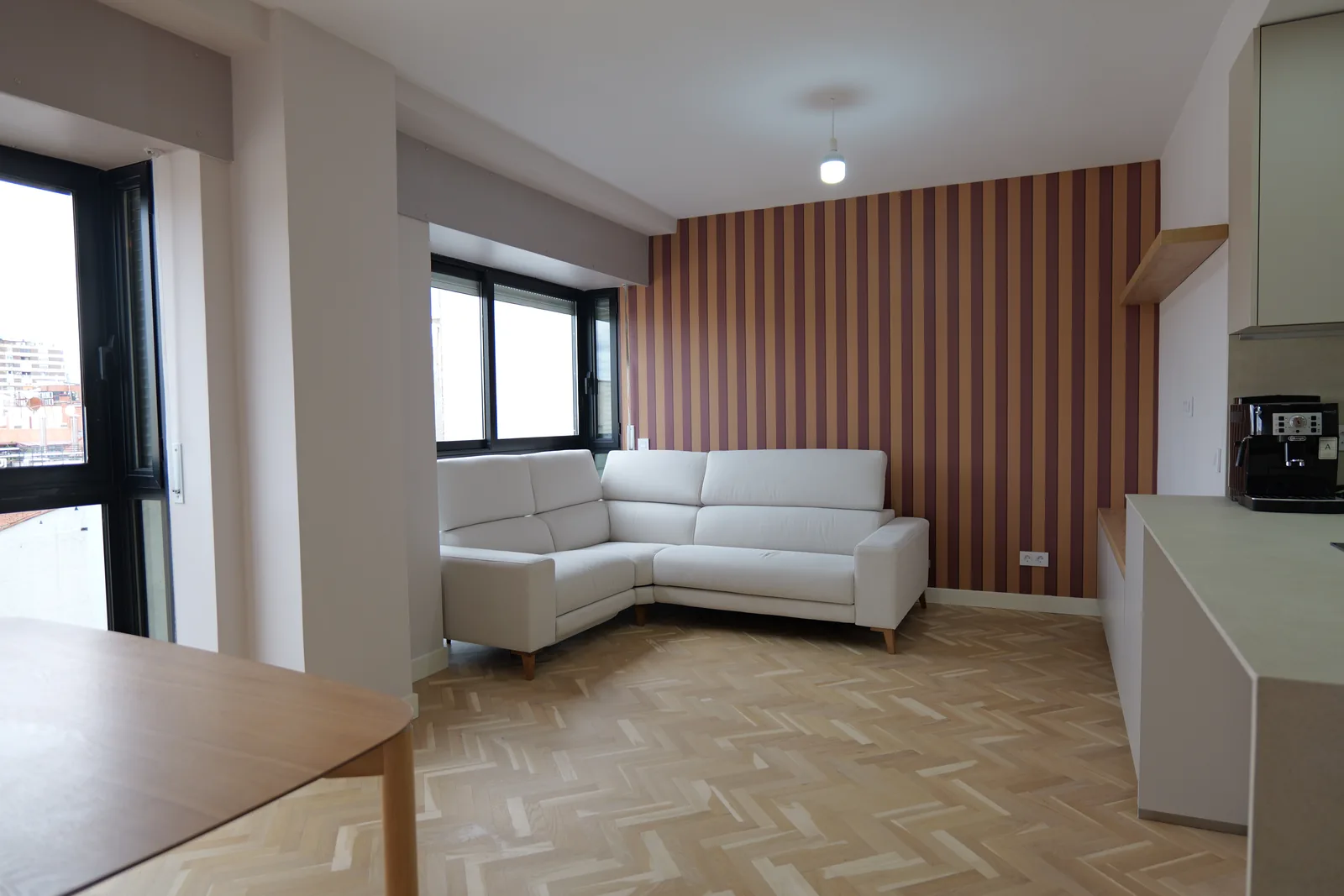 Salón con sofá rinconera blanco, pared de papel pintado a rayas y suelo de madera en espiga