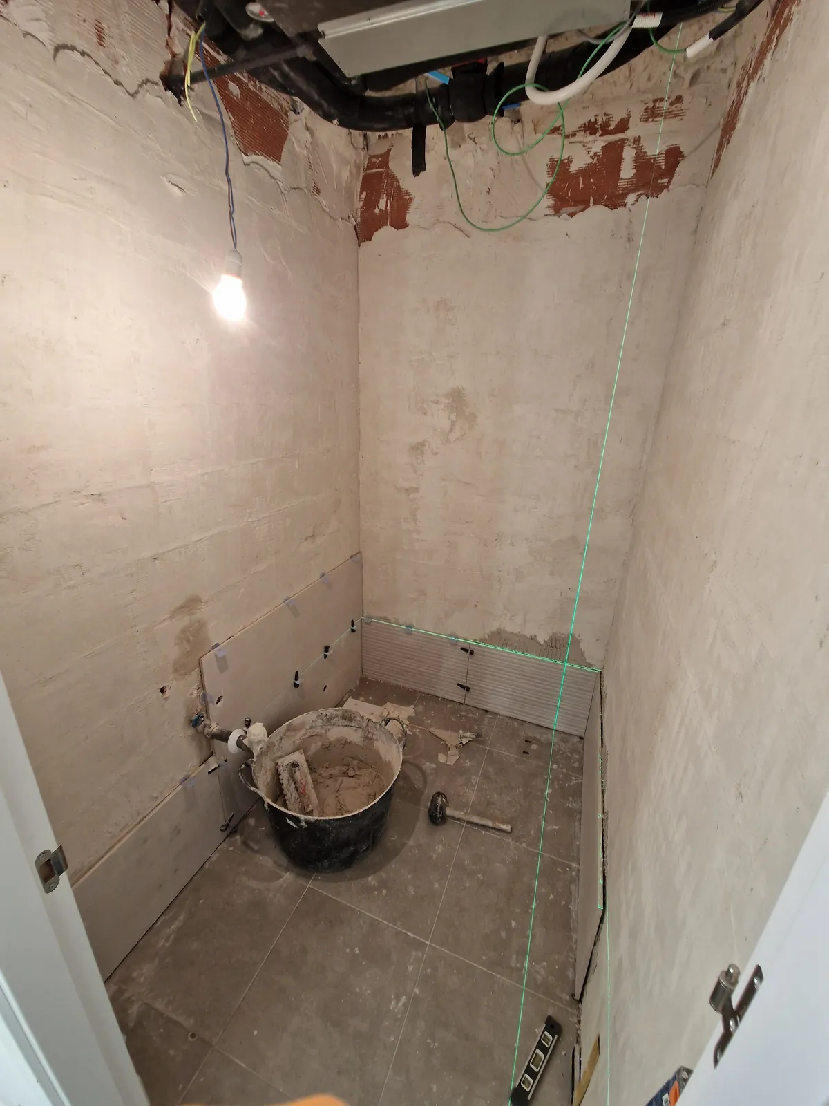 Baño durante la obra con instalaciones abiertas en el techo y revestimiento nuevo