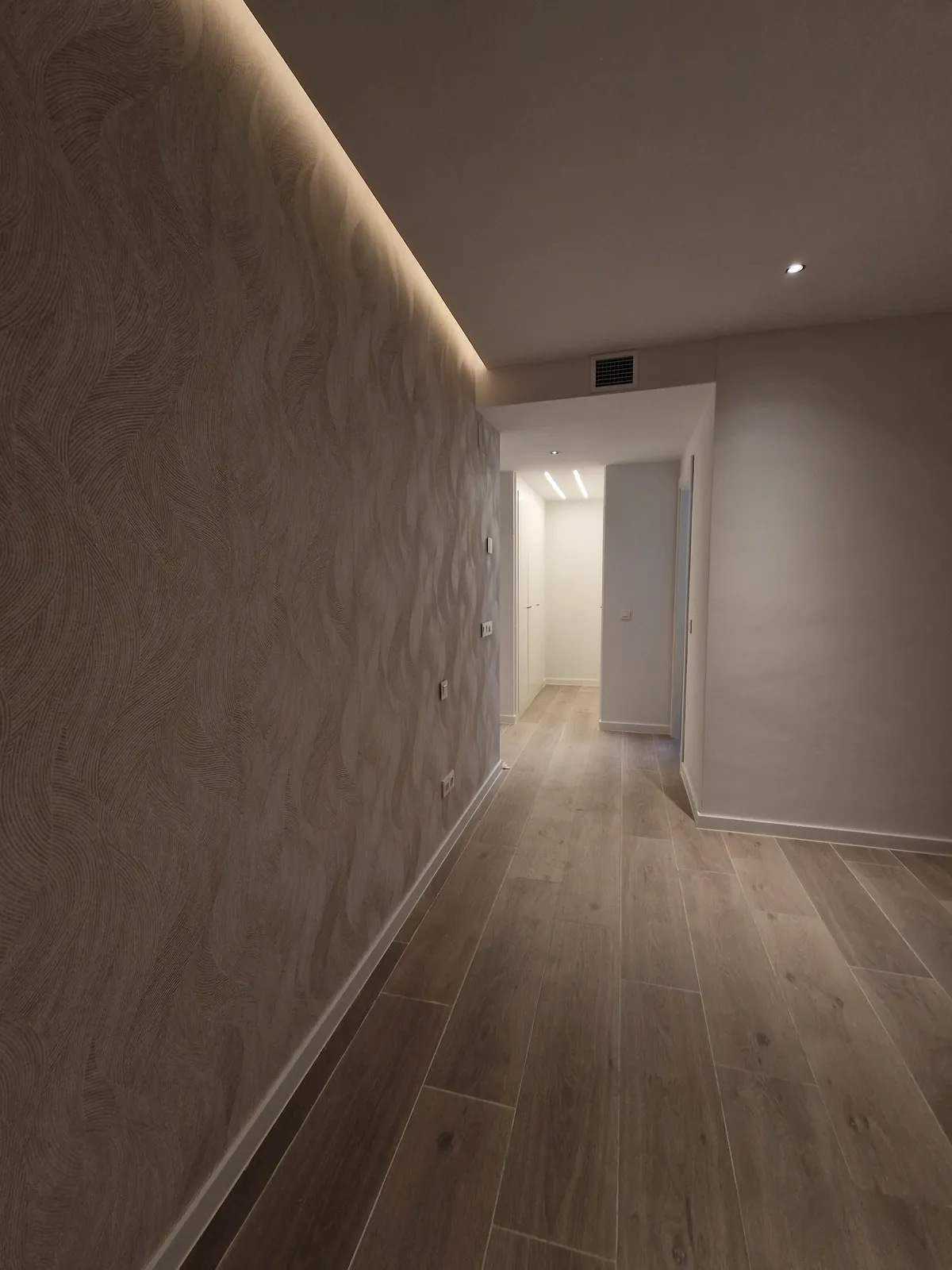Pasillo con revestimiento decorativo en relieve, luz LED indirecta en el techo y suelo tipo madera