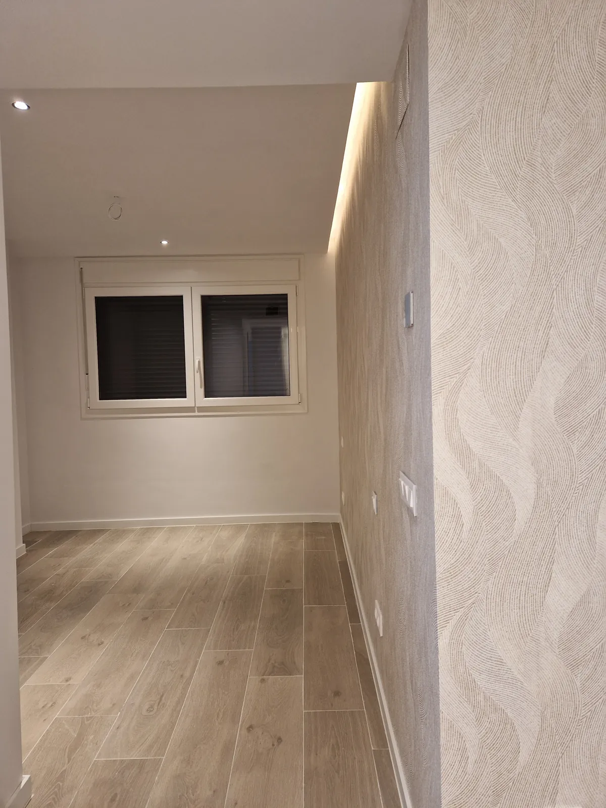 Estancia con pared de relieve ondulado, tira de luz en el techo y suelo porcelánico tipo madera