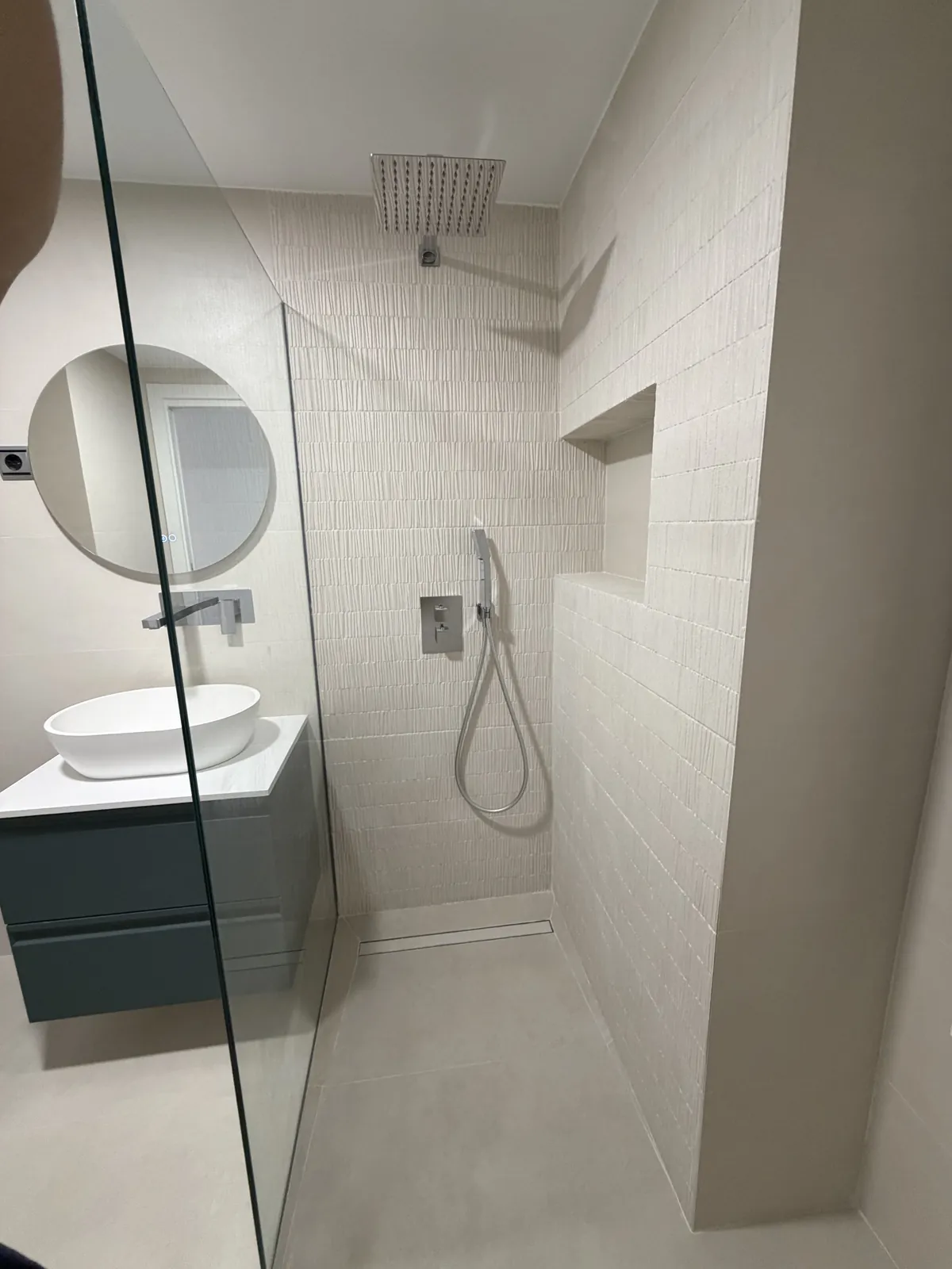Segundo baño en tonos claros con mampara de vidrio, espejo redondo y lavabo sobre mueble suspendido