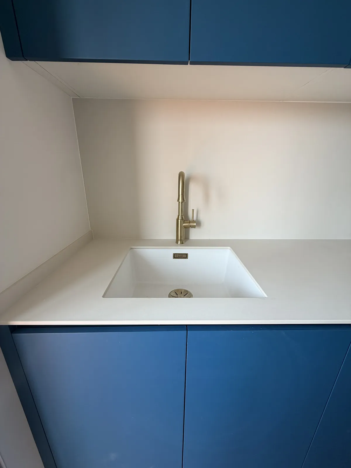Detalle de fregadero bajo encimera blanca con grifo dorado y muebles azules