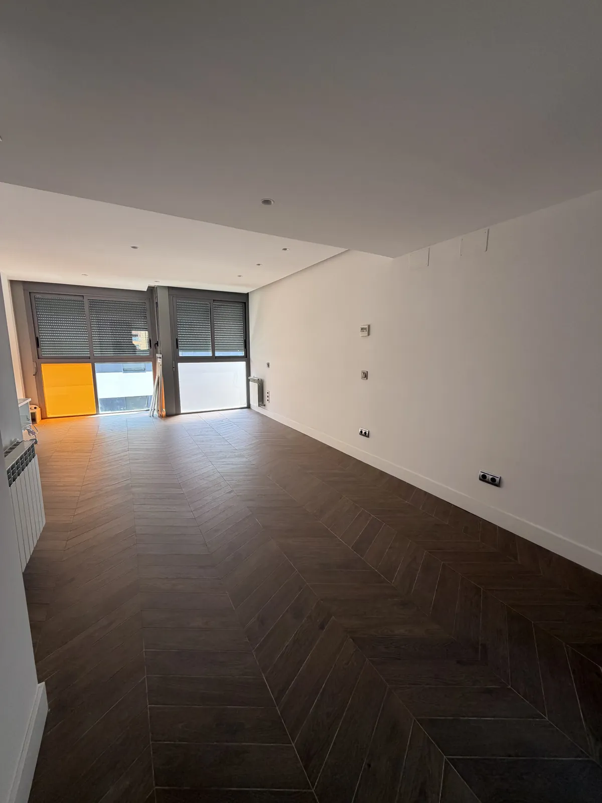 Salón vacío tras la reforma con suelo tipo madera en espiga y paredes blancas