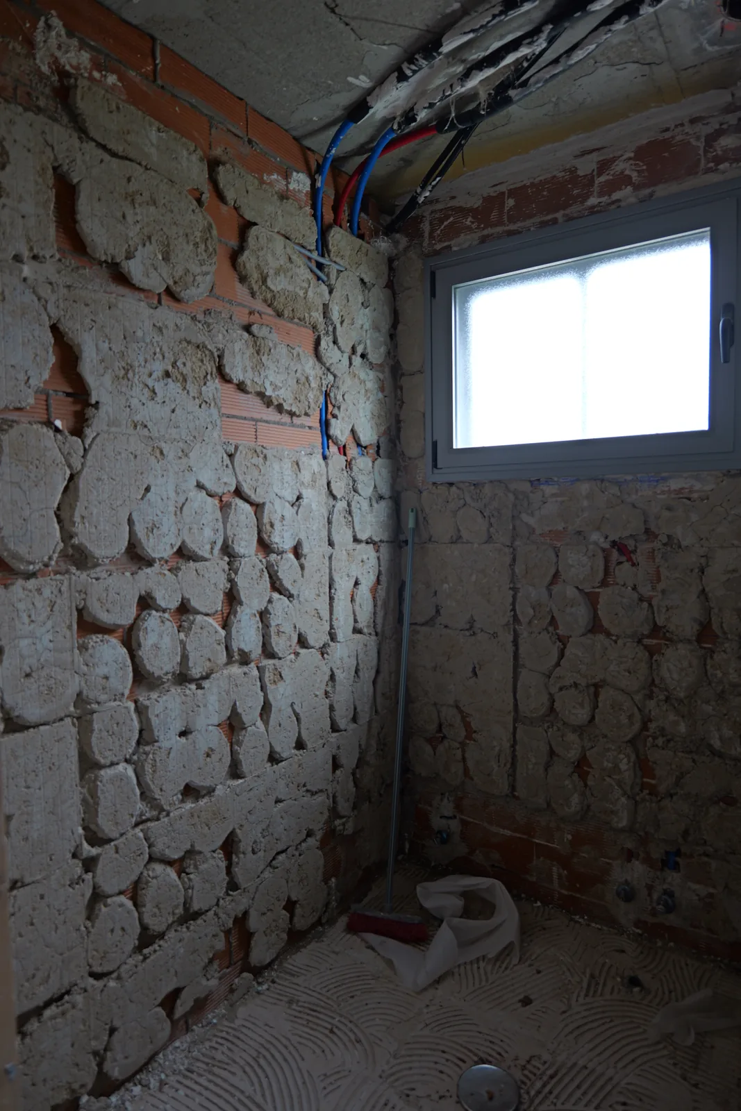 Baño en fase de demolición con paredes picadas e instalaciones nuevas en el techo