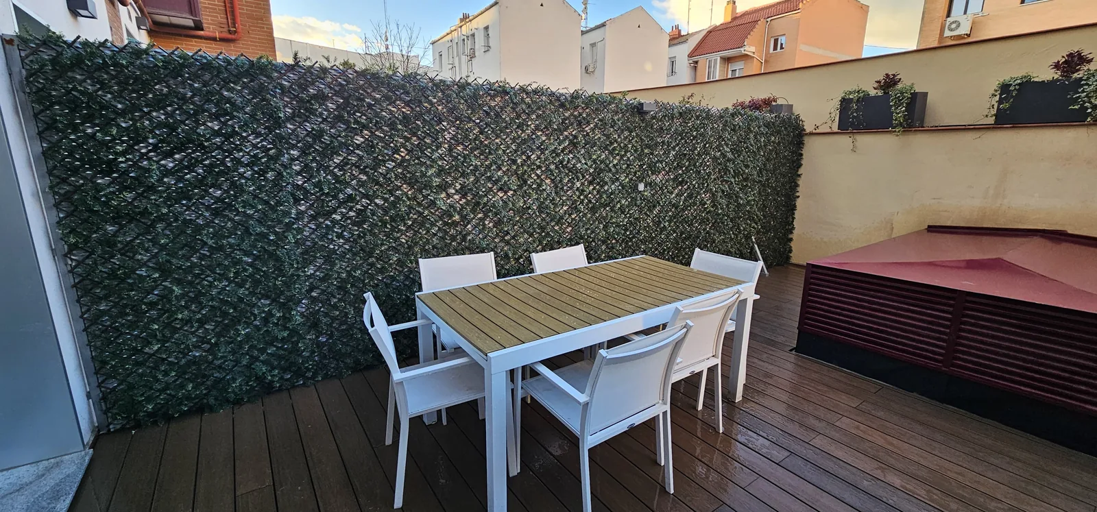 Patio con tarima exterior de madera, cerramiento vegetal artificial y mesa de jardín