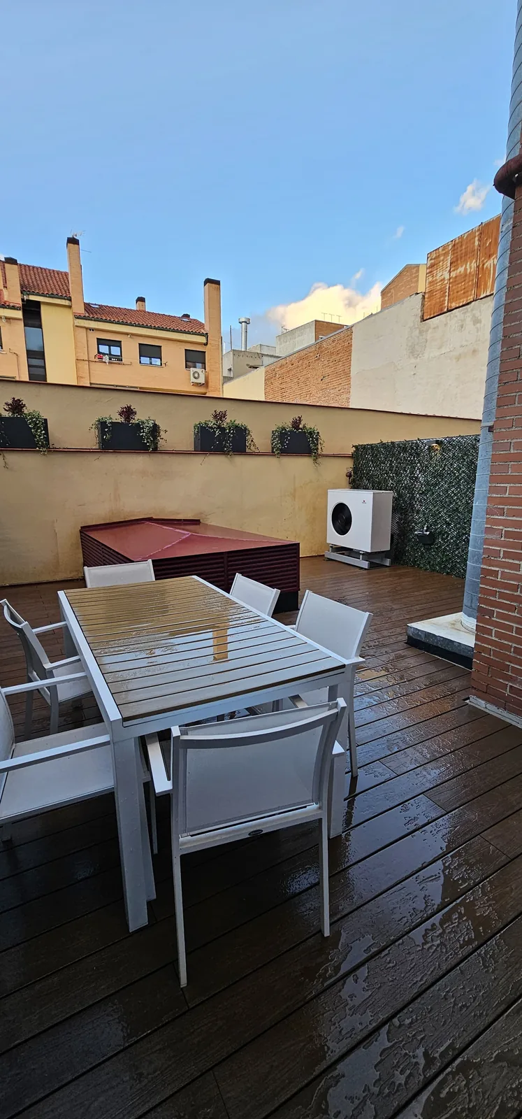 Vista vertical del patio con tarima de madera, jardineras y mesa exterior