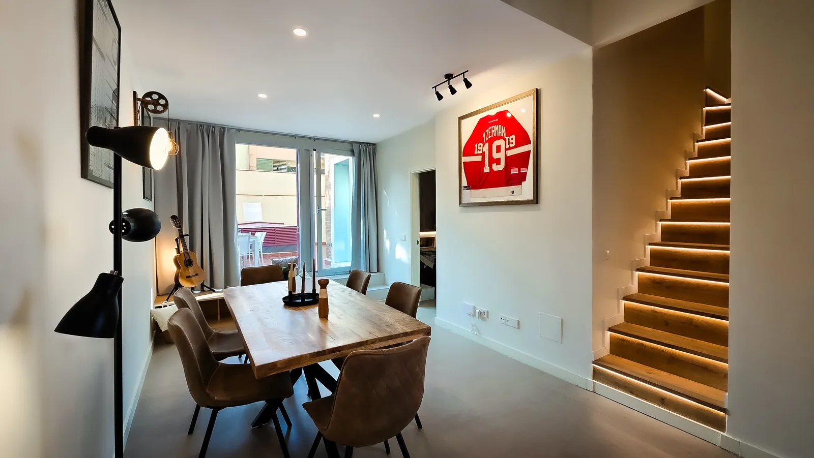 Salón-comedor del loft con mesa de madera y escalera de peldaños de madera con iluminación LED