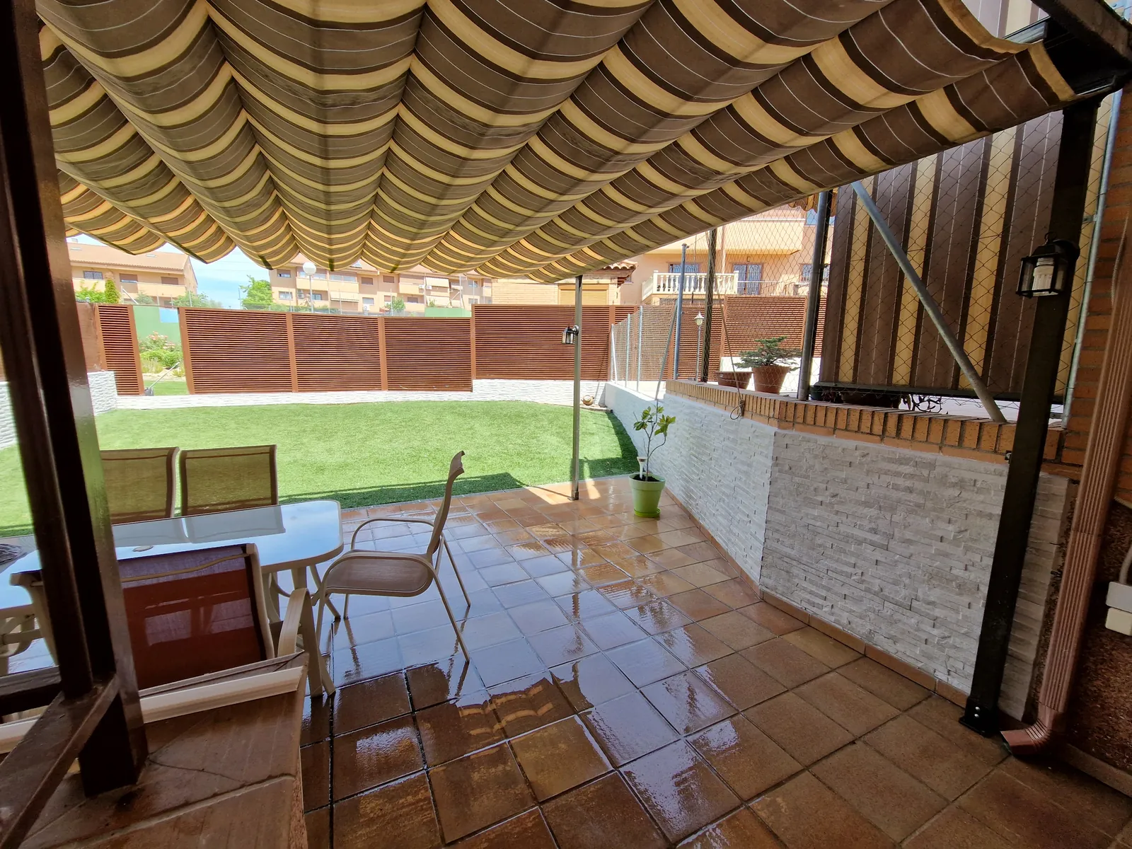 Porche con murete de piedra blanca, toldo plegable y jardín