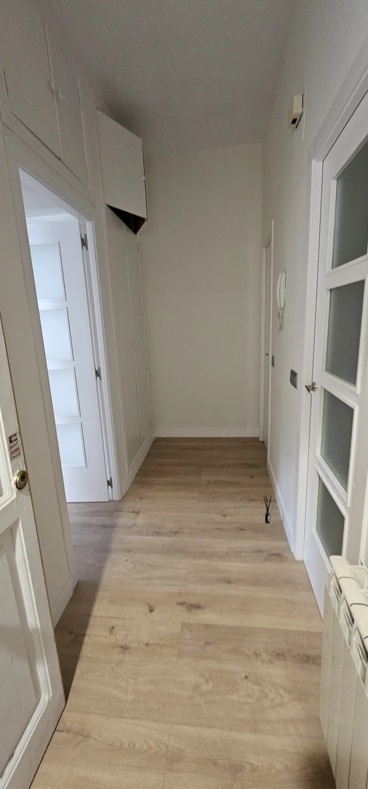 Pasillo pintado en blanco con suelo laminado de roble claro y puertas blancas con vidriera
