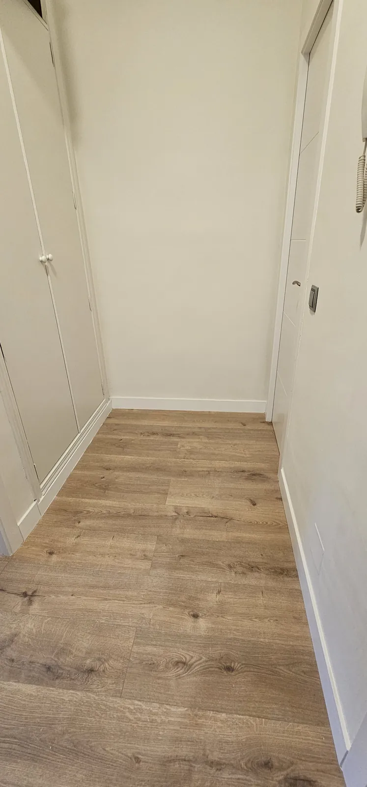 Pasillo con suelo laminado tipo madera y rodapié blanco tras la reforma
