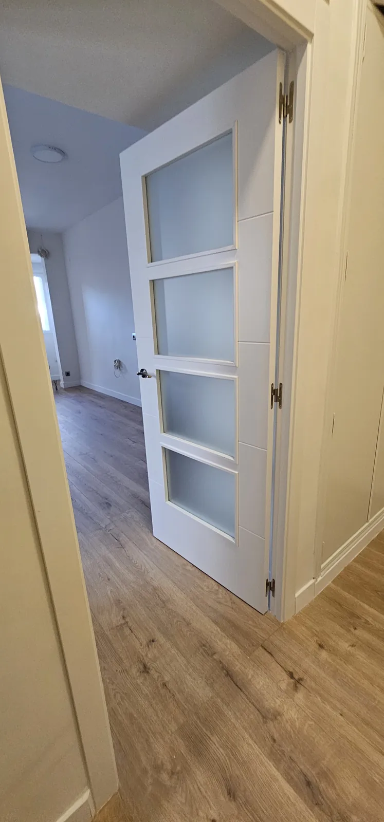 Puerta interior blanca con vidriera abierta hacia una estancia con suelo laminado