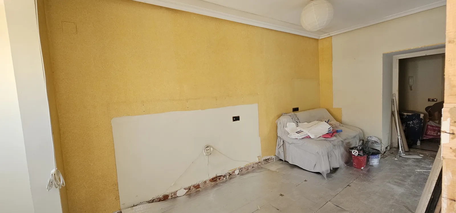 Estancia antes de la reforma con pared amarilla y suelo sin terminar